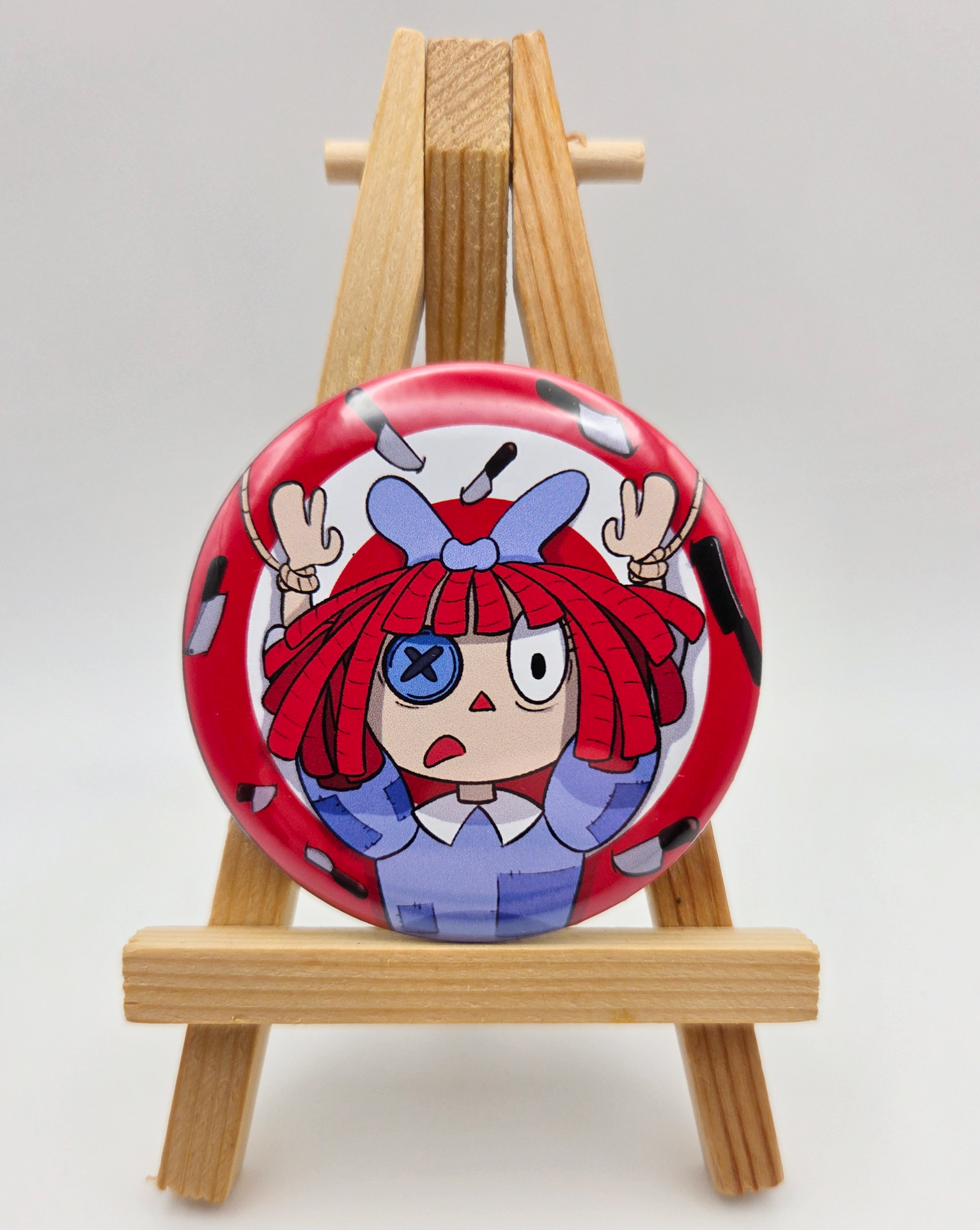 A button featuring RAGATHA from THE AMAZING DIGITAL CIRCUS resting on a small easel.