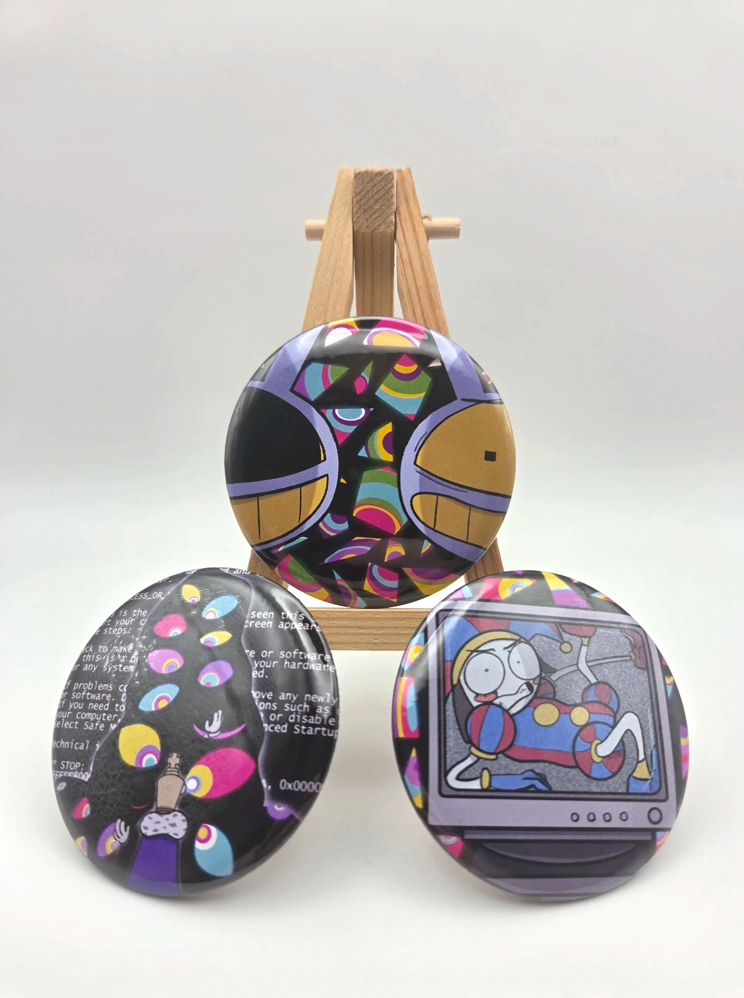 Three buttons featuring characters from THE AMAZING DIGITAL CIRCUS sitting on an easel.
