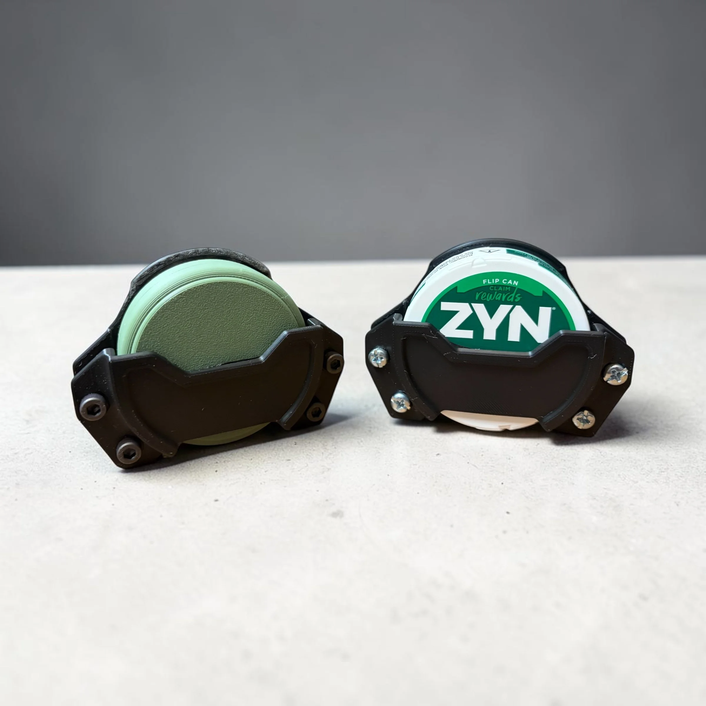 Two small bottles of ZYN nicotine pouches with green and white labels, placed on a white surface, against a plain gray background.