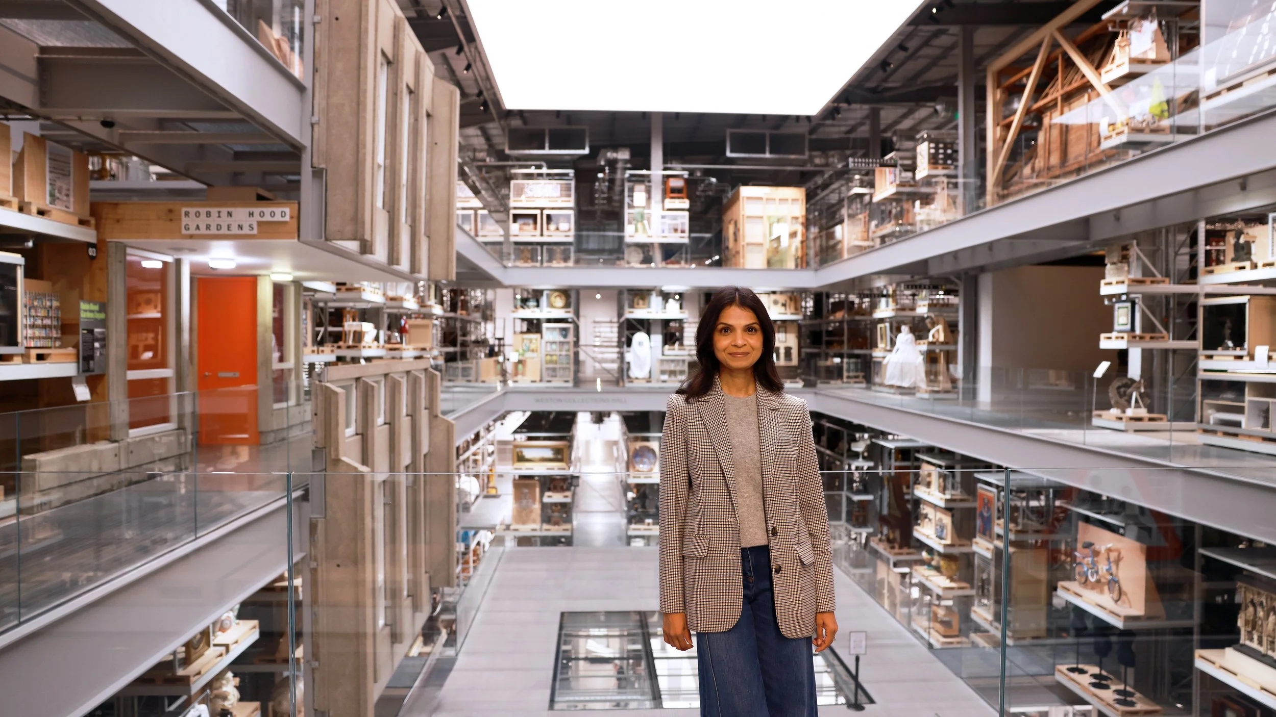 A woman in a business blazer and jeans standing in a multi-story modern bookstore or library with open shelves and artworks on display.