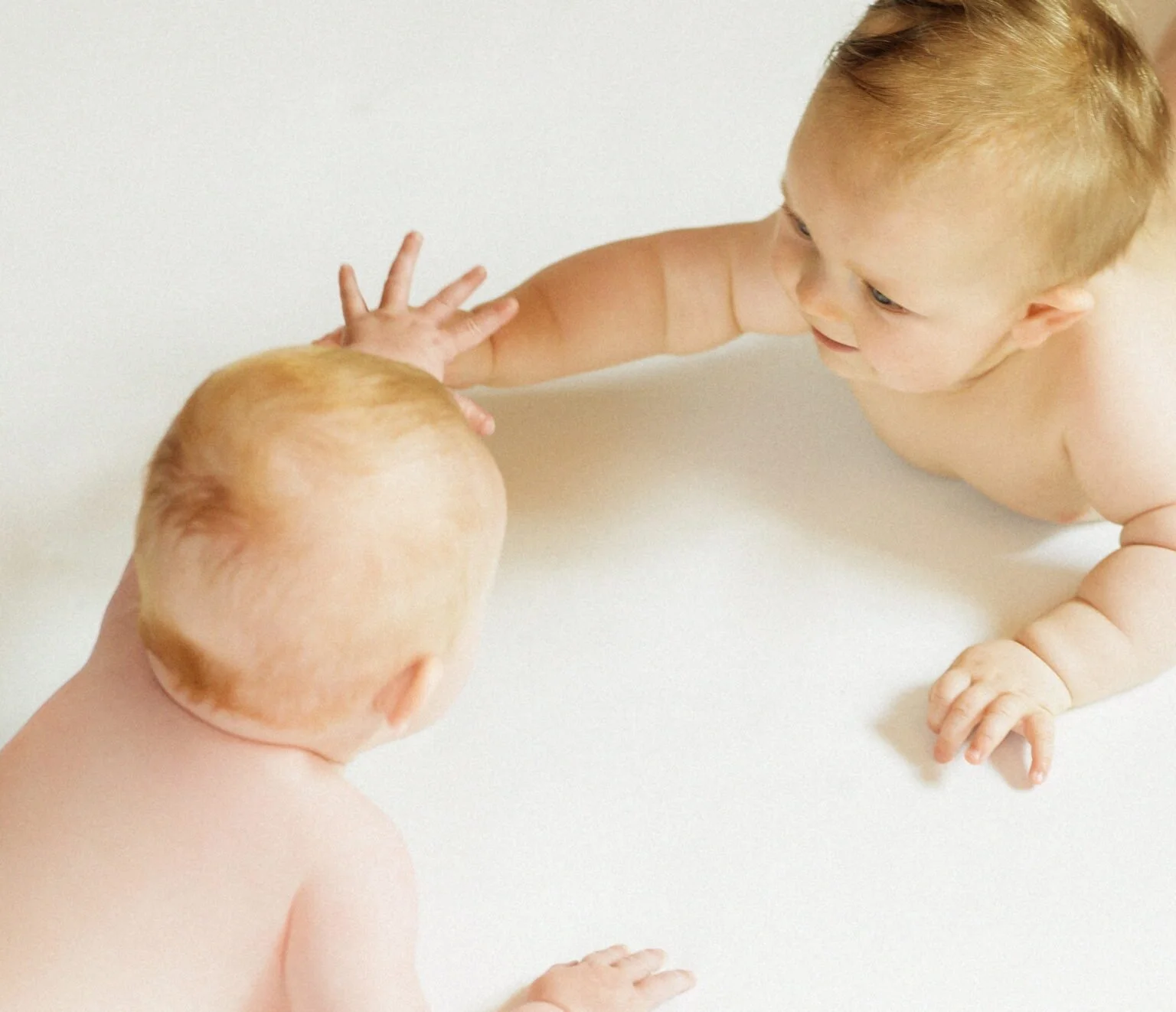 Zwei nackte Babys, die sich im Wasser gegenüberliegen und sich gegenseitig berühren.