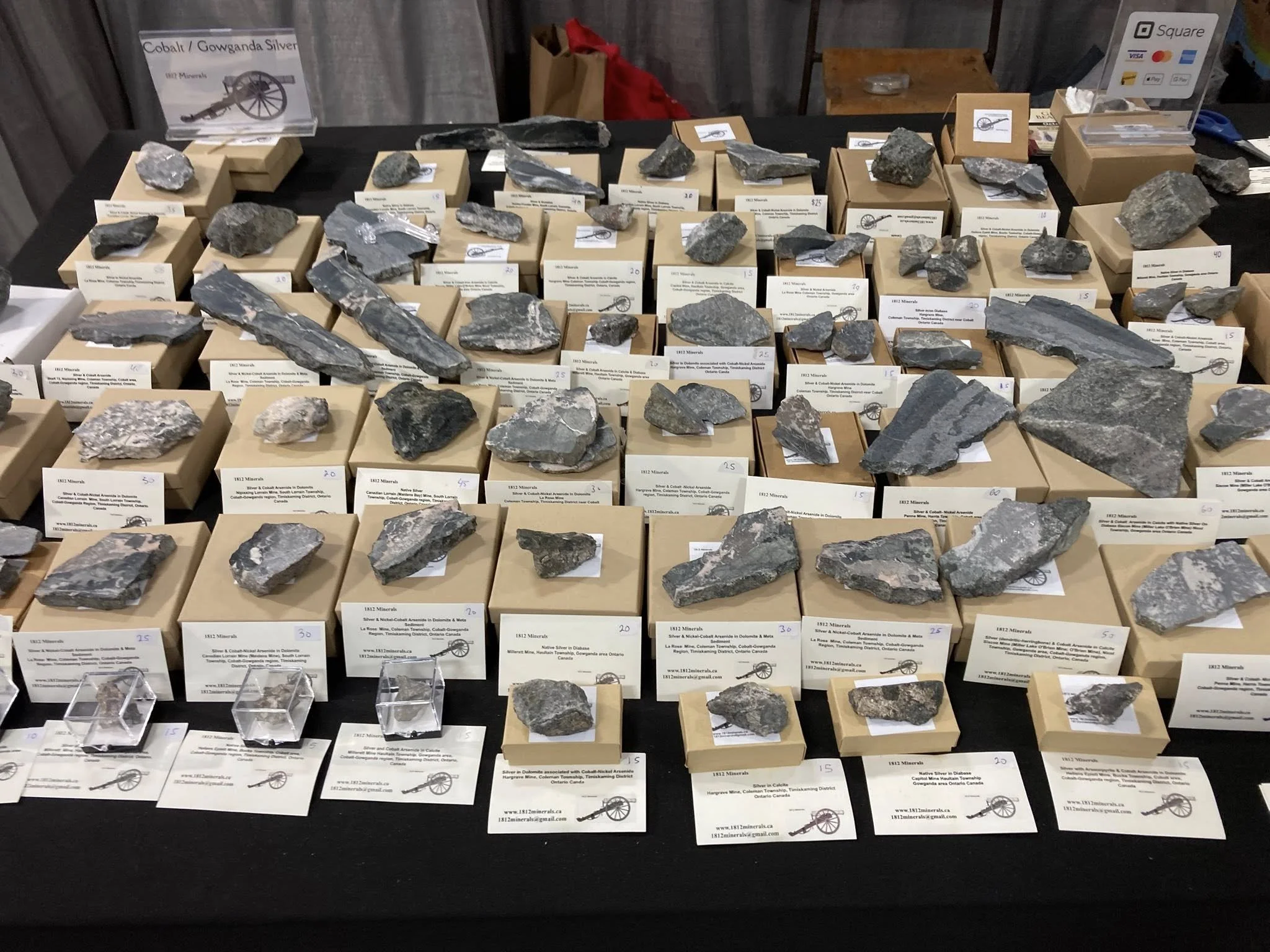 Display table with various mineral rocks, each labeled with tags and prices, at a mineral exhibit.