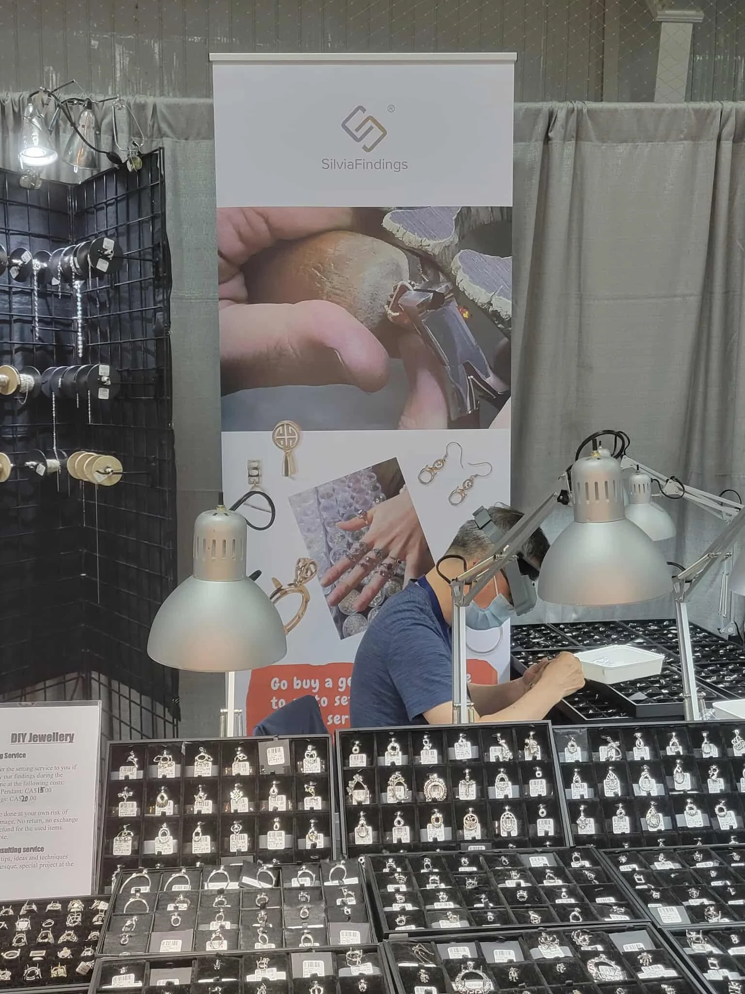 Display of jewelry with a person working on jewelry pieces at a jewelry booth at a craft fair or market.