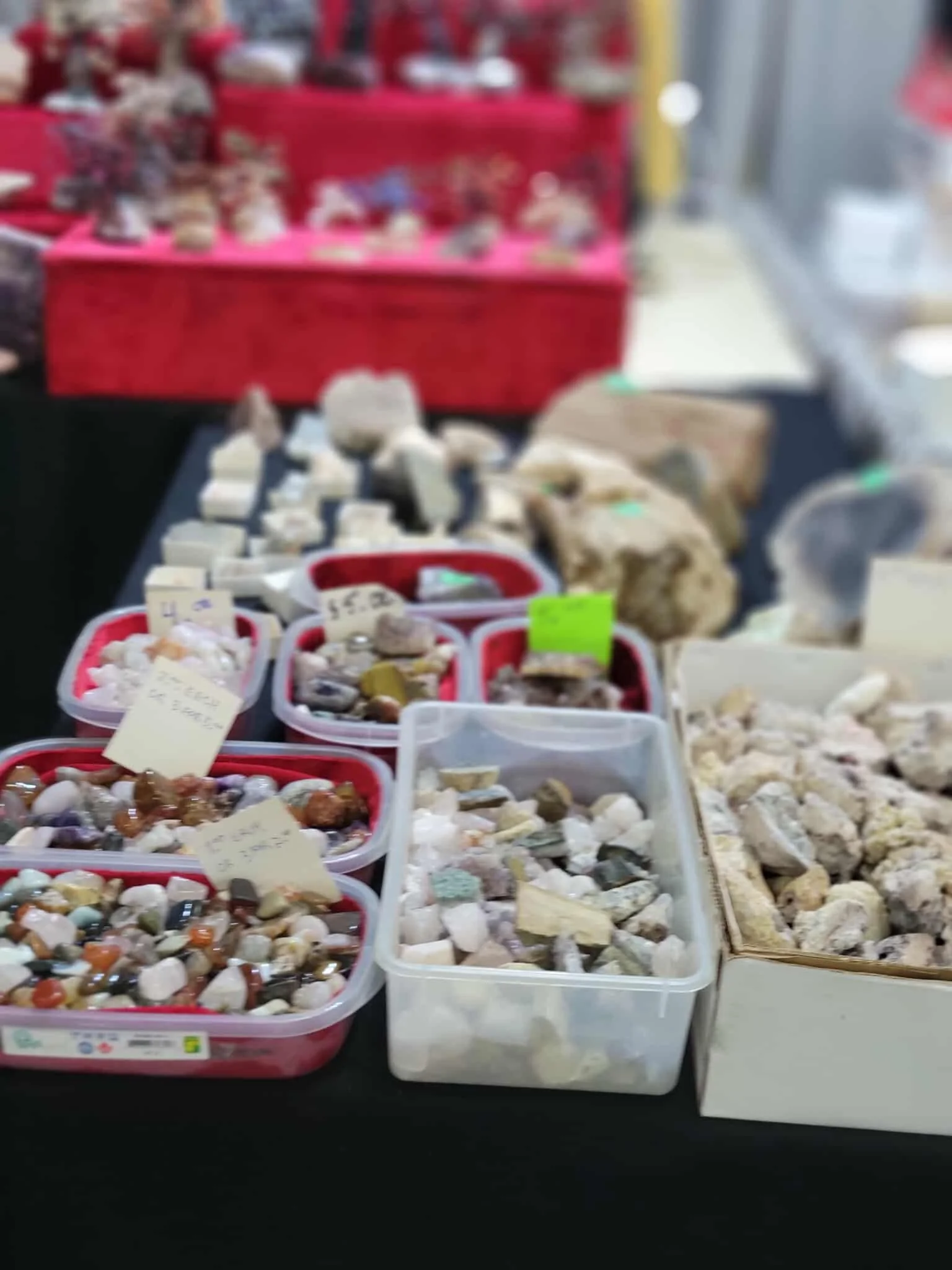 Display of various polished stones and minerals in plastic containers at a market stall.