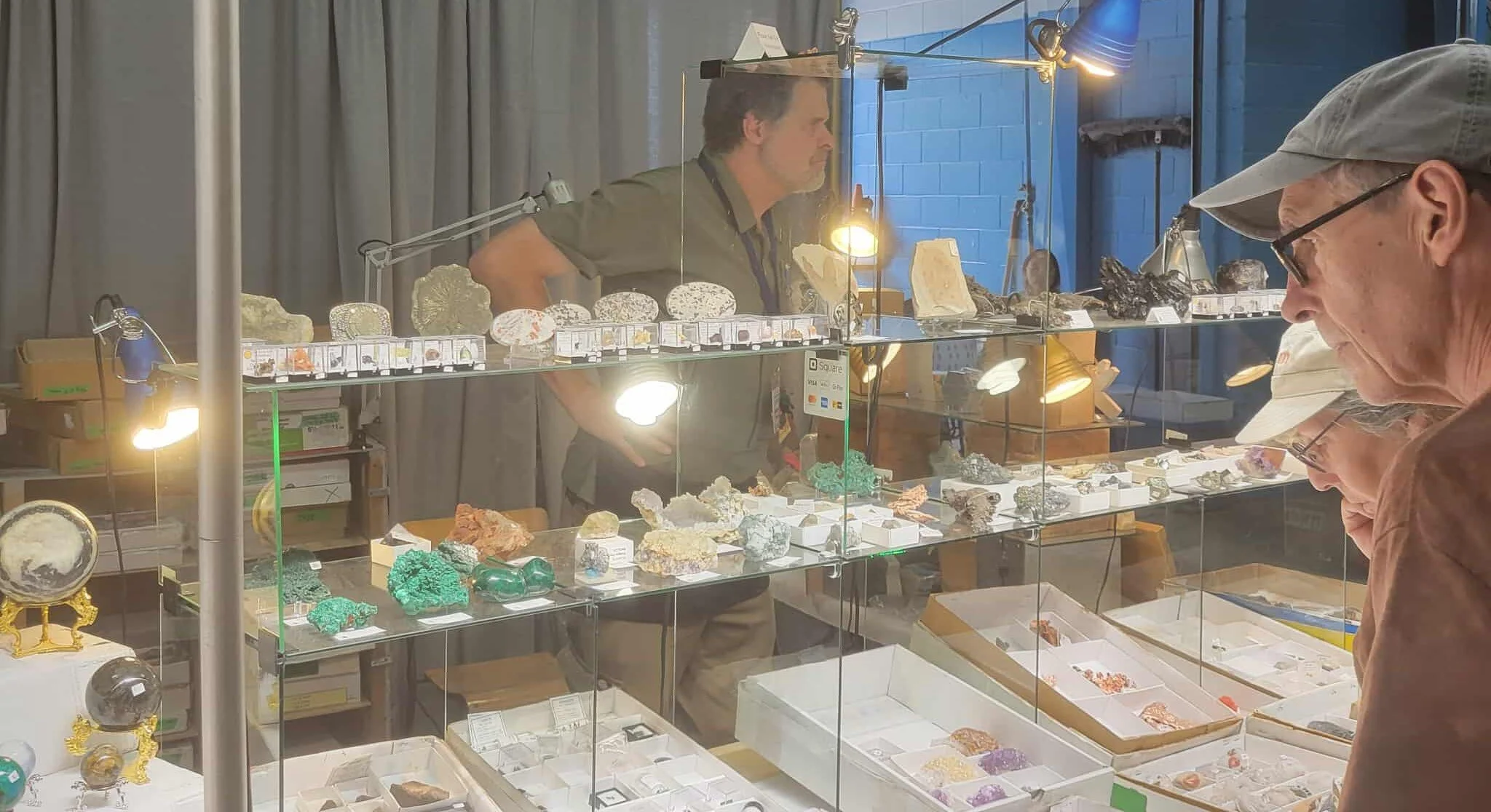Display case at a mineral and gemstone exhibit with various rocks and minerals, and visitors viewing the display.