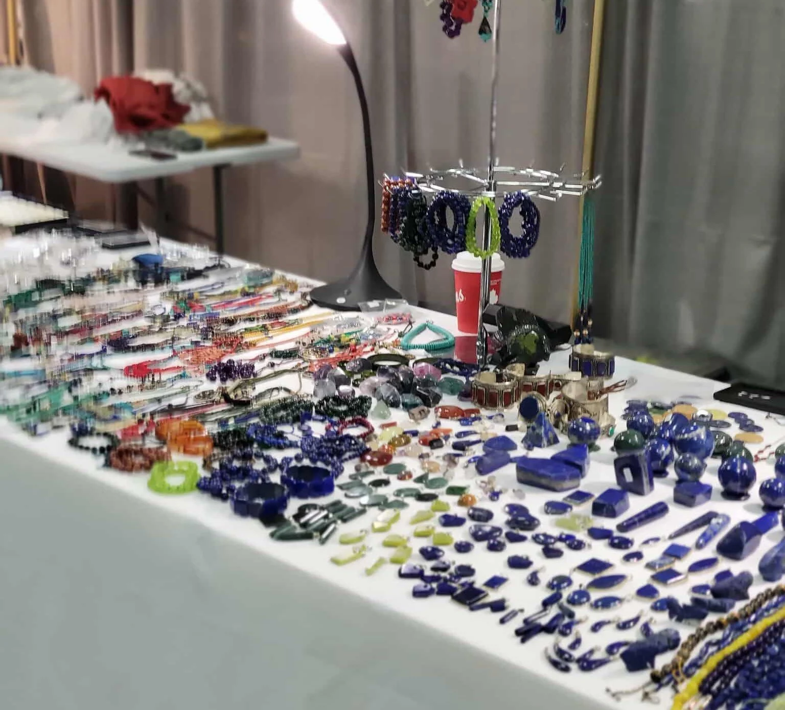 A display table filled with colorful jewelry including bracelets, rings, necklaces, and beaded accessories at a craft or jewelry fair.