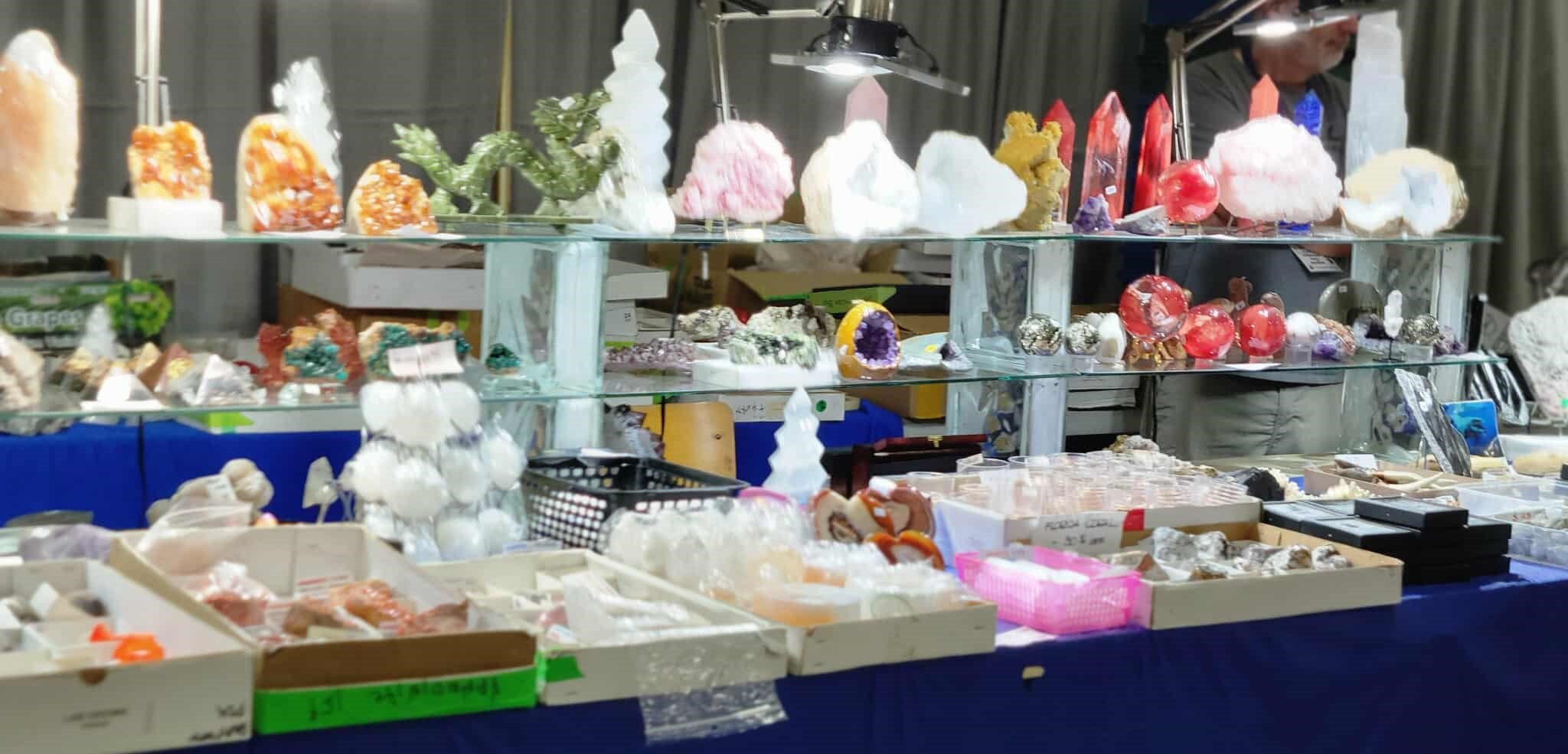 Display of various mineral and crystal specimens at a market stall, with a person behind the table.