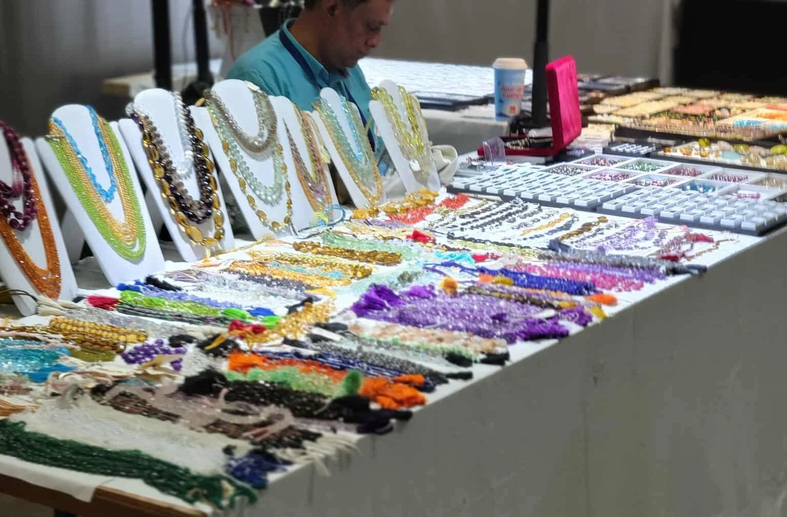Jewelry booth displaying colorful necklaces, bracelets, and earrings on white stands and displays.
