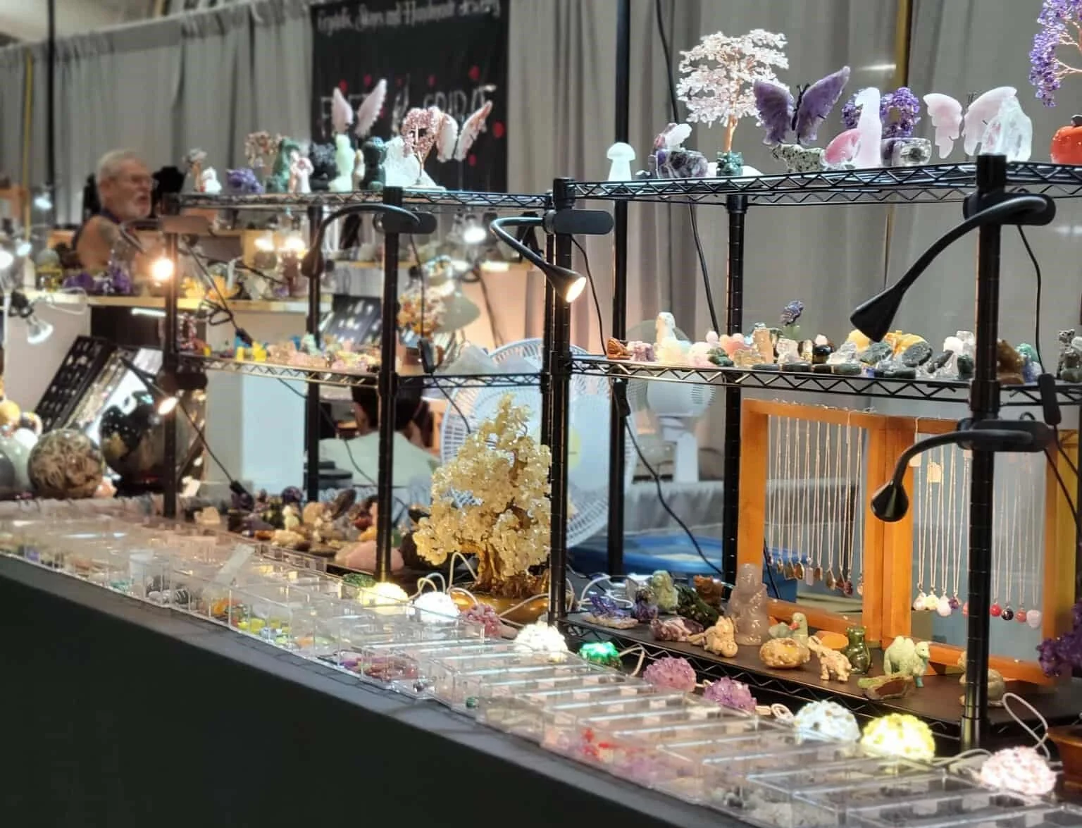 Display of handcrafted minerals, crystals, and jewelry at a vendor booth, with shelves and tables showcasing various stone and mineral specimens.