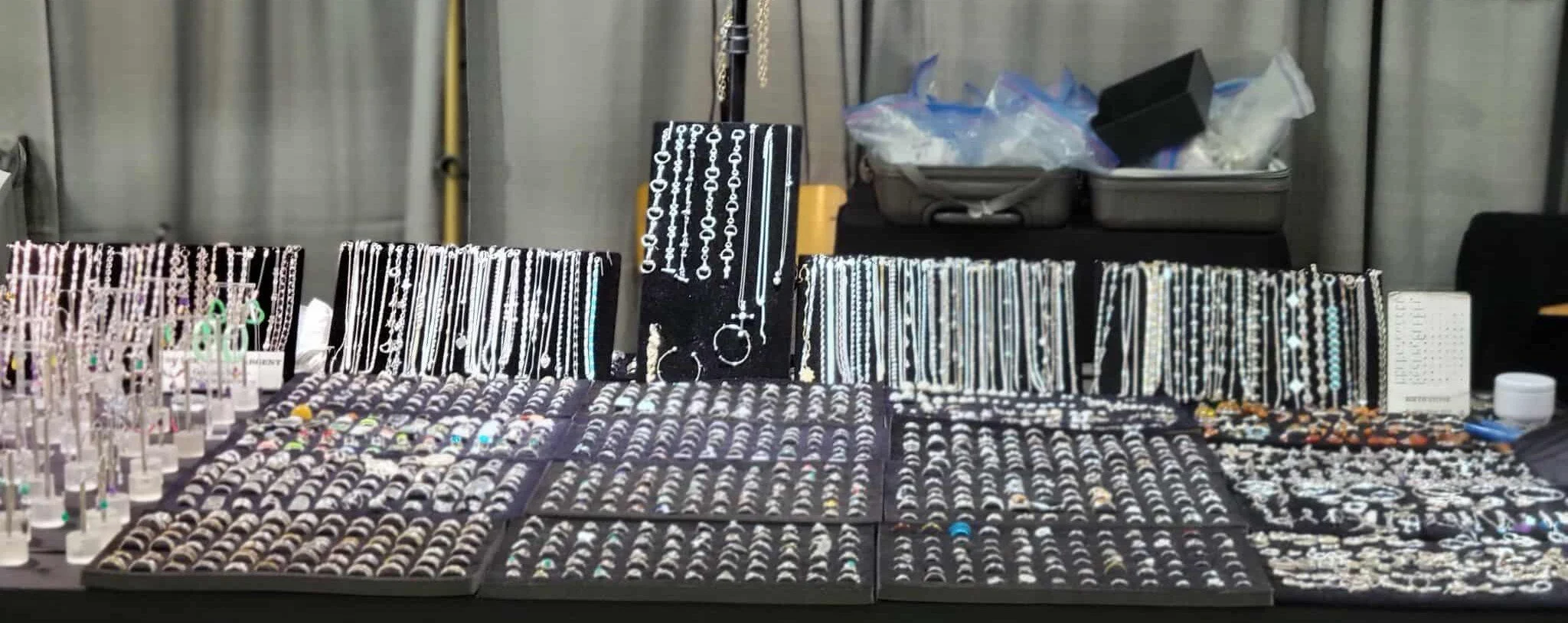 Jewelry display table with various rings, earrings, necklaces, and bracelets, set up at a market or fair.