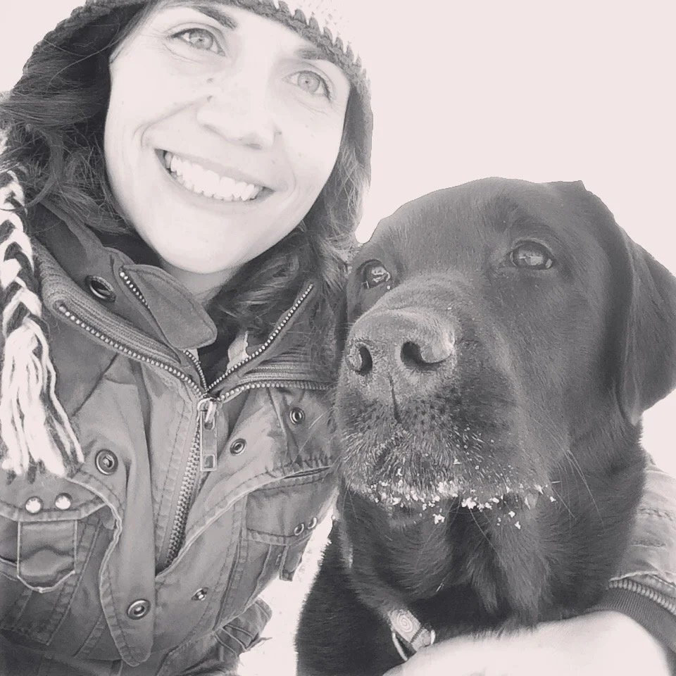 A woman smiling with a black dog in a snowy environment.