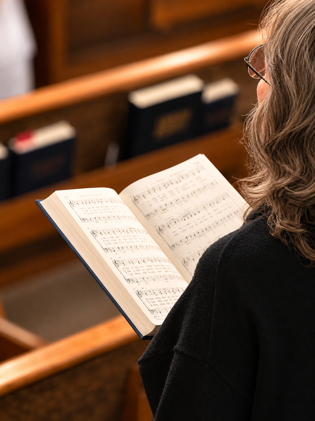 A woman with glasses and curly hair reading sheet music in a church or concert hall.