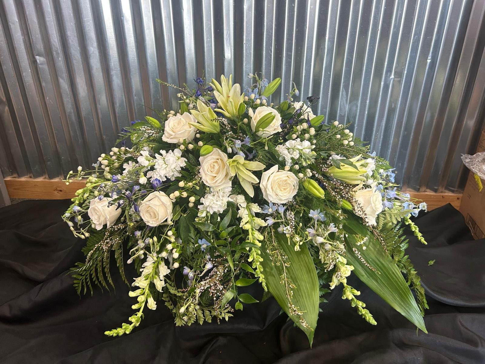 Med sized Casket Spray ft white lilies, roses and white snapdragons.