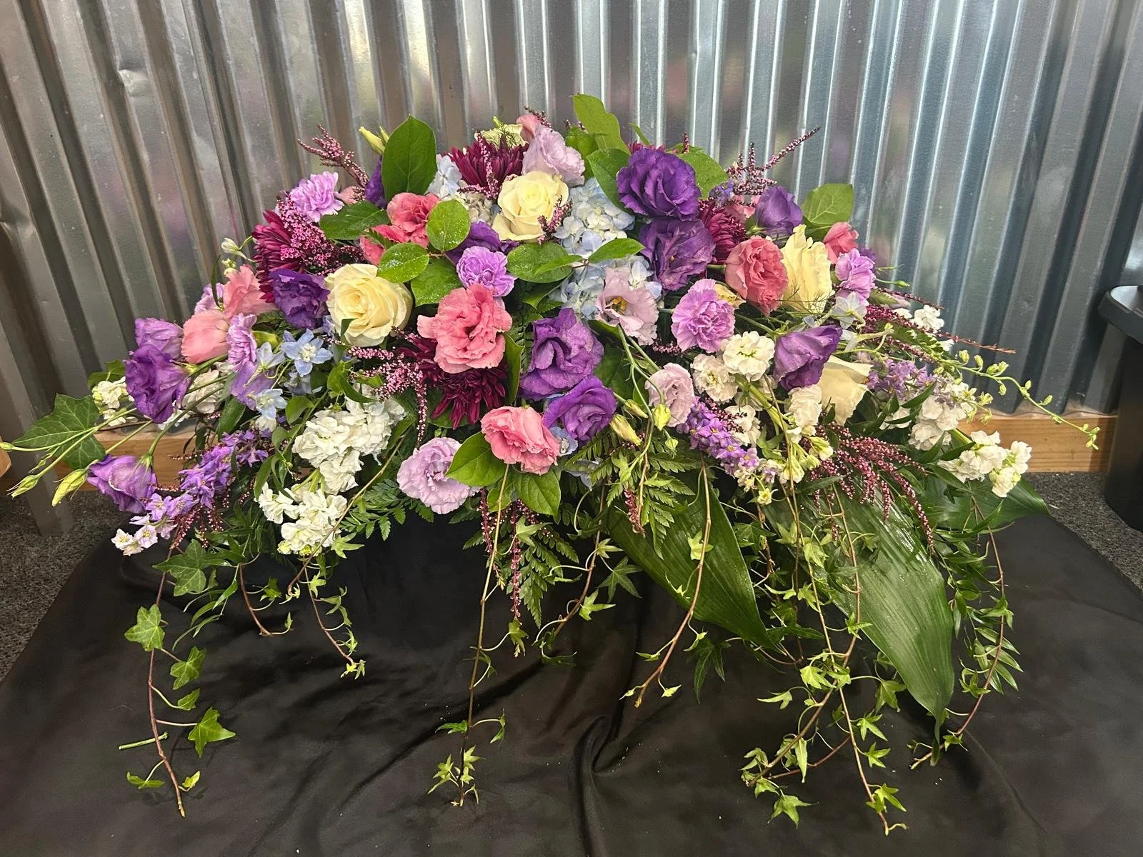 Med sized Casket spray ft, purple lisisanthus and trailing ivy.