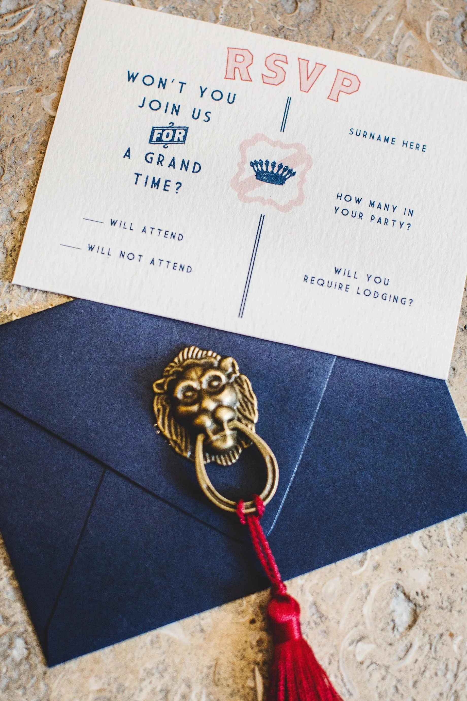 A wedding RSVP card with questions about attendance, party size, lodging, and a decorative lion-shaped envelope clip with a red tassel attached.