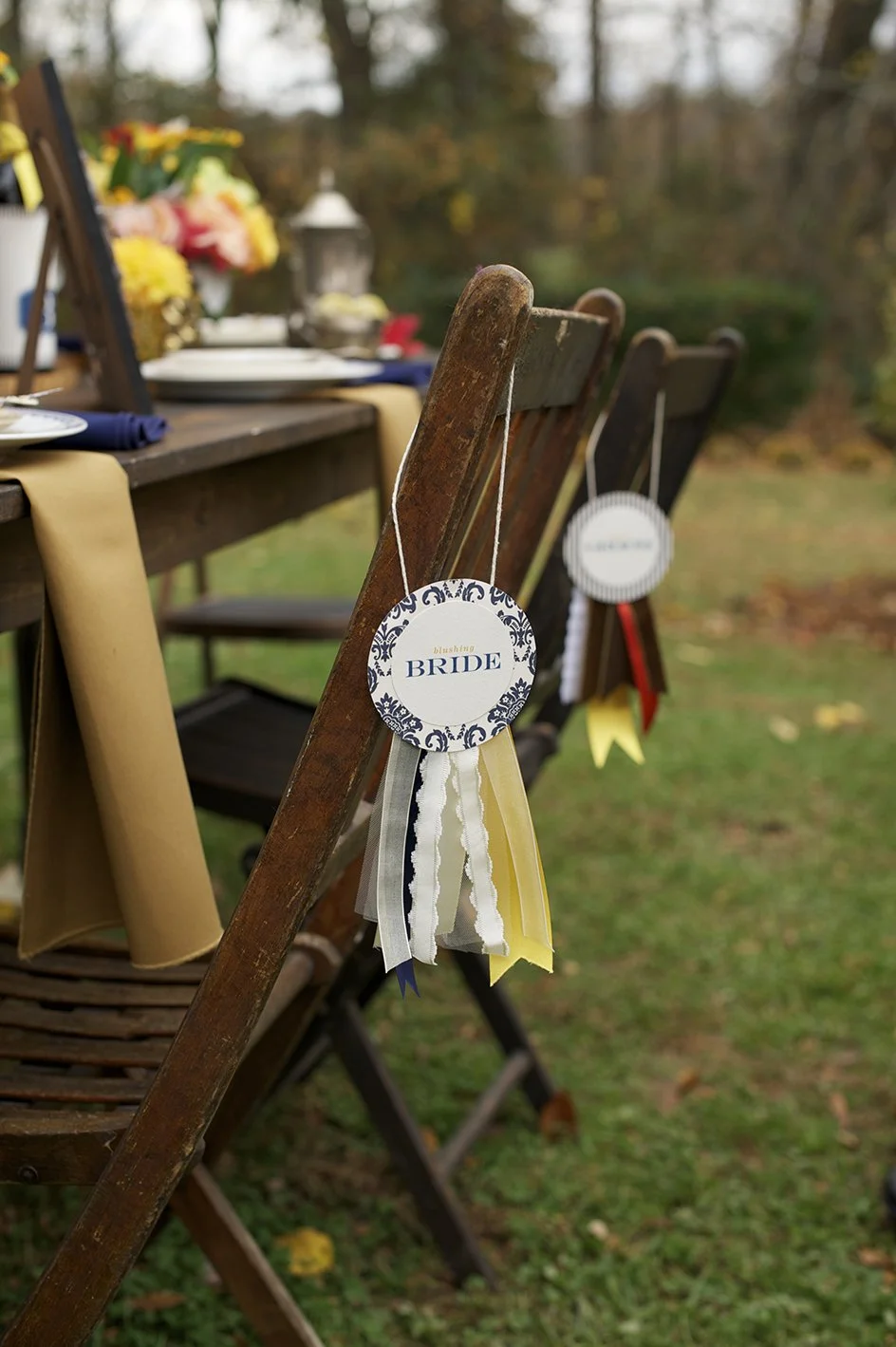 Outdoor wedding table setting with wooden chairs decorated with ribbons and a circular tag that says 'blushing BRIDE'.