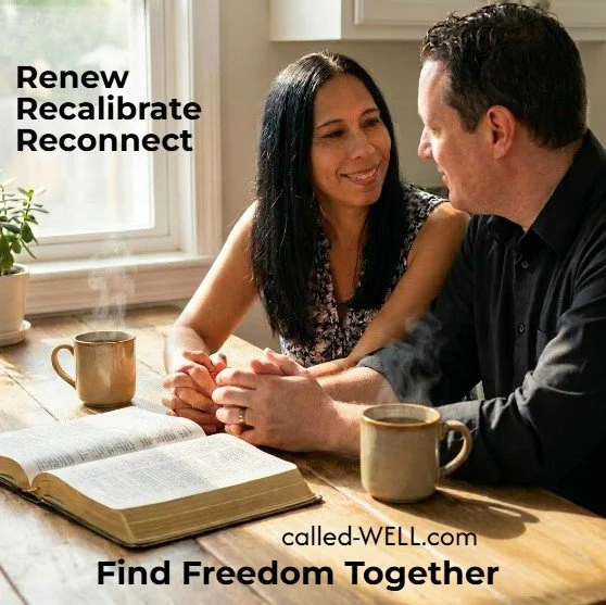 A woman and a man sitting at a wooden table, holding hands and smiling at each other, with open books and coffee mugs on the table, near a window with sunlight.