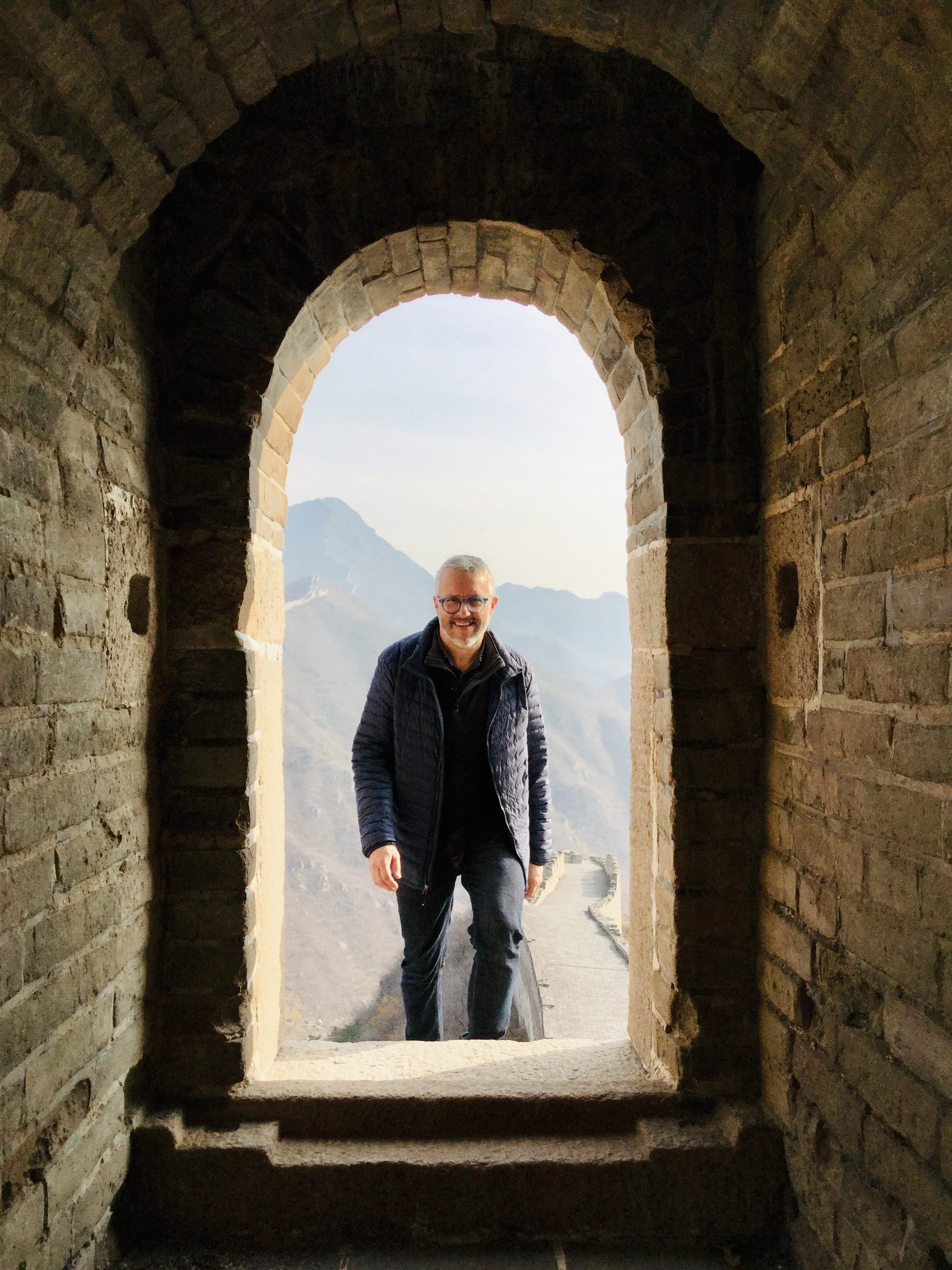 A man walking through a stone archway with mountains in the background.