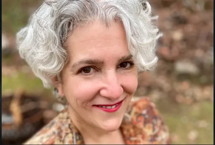 Close-up of a smiling woman with short, curly gray hair outdoors.