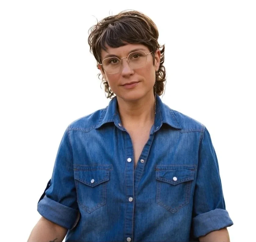 A woman with short brown hair, wearing glasses and a blue denim shirt, looking at the camera with a slight smile.