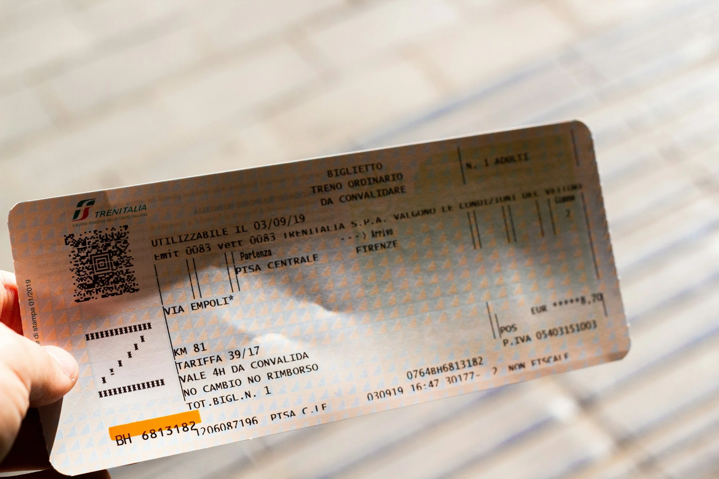 Italian train ticket with the 'Trenitalia' logo, containing details about journey, date, and fare, held in a person's hand.