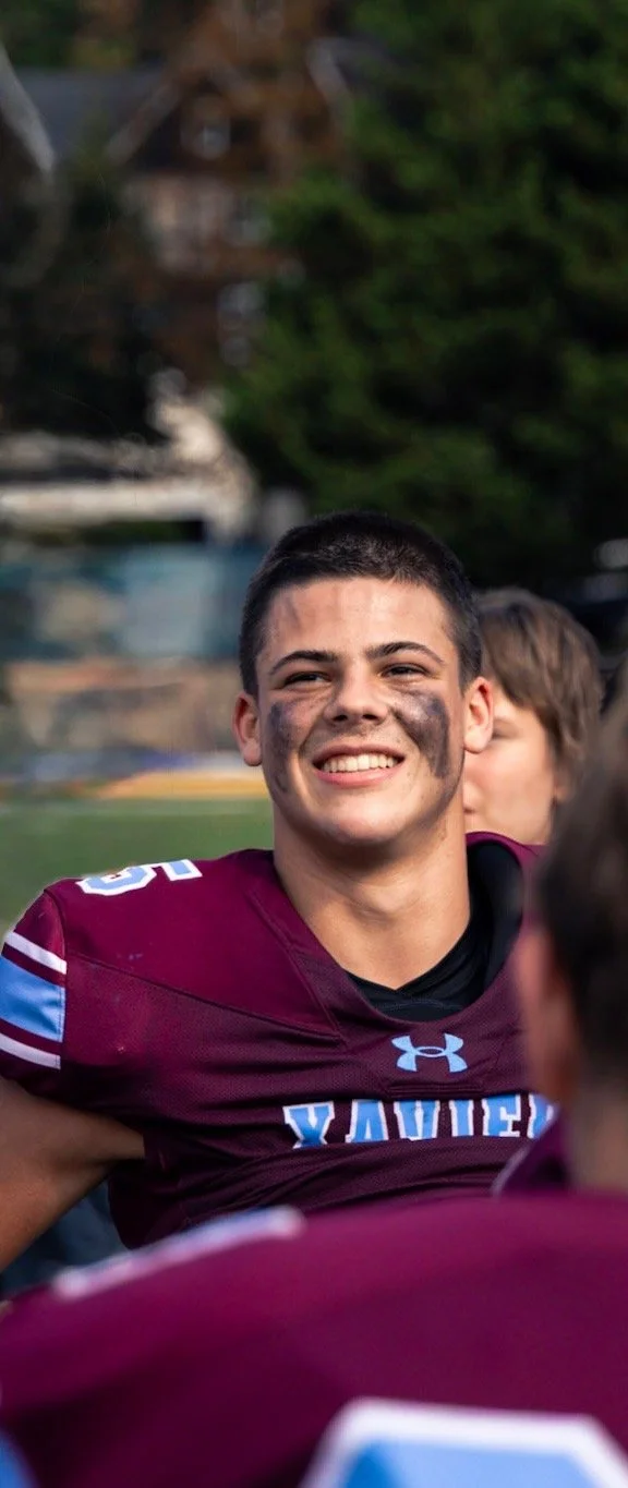 A young male football player with short dark hair and face paint, smiling, wearing a maroon jersey with blue and white accents.