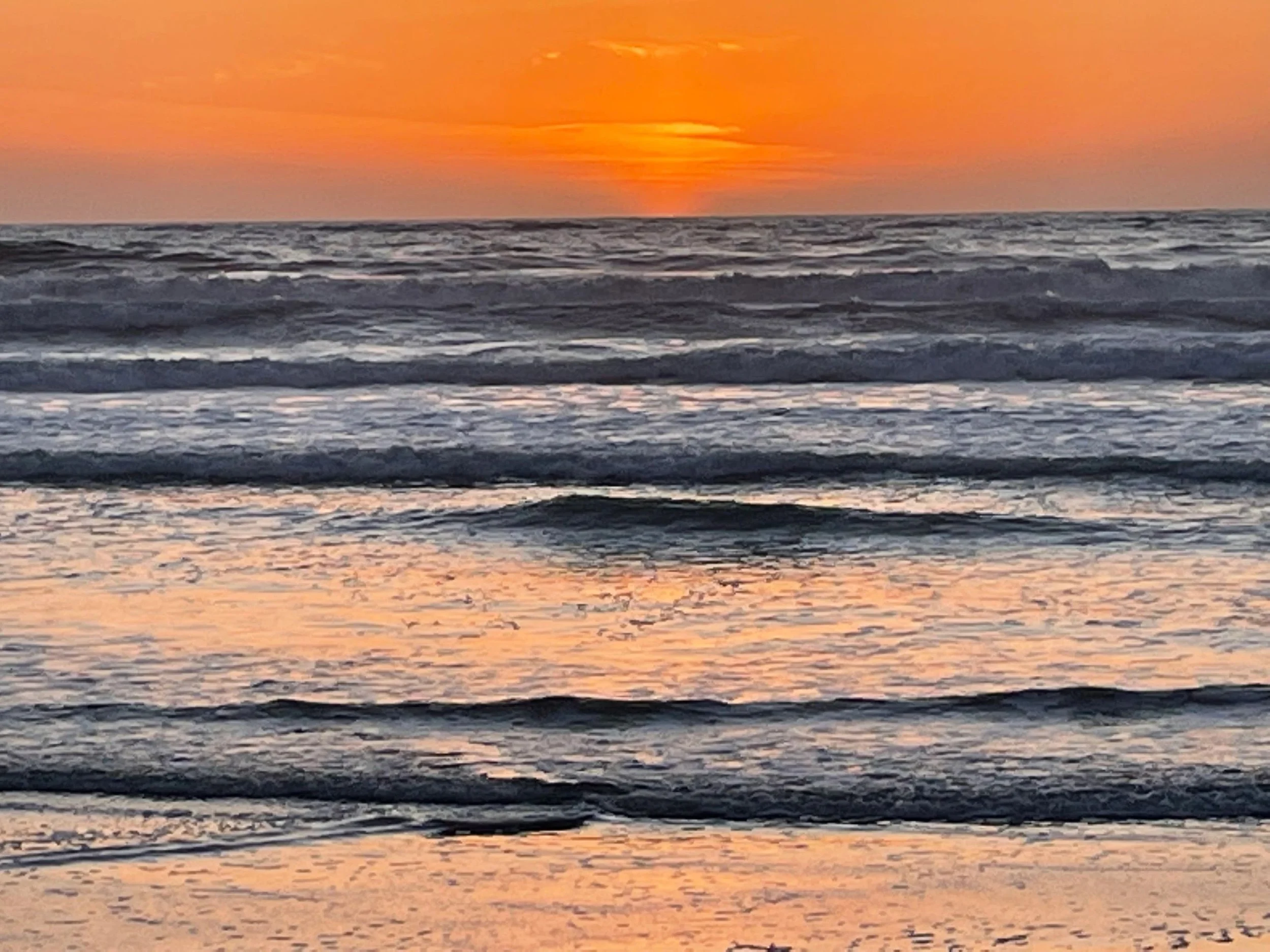 Sunset over the ocean with waves gently crashing on the shore, orange sky with some clouds.