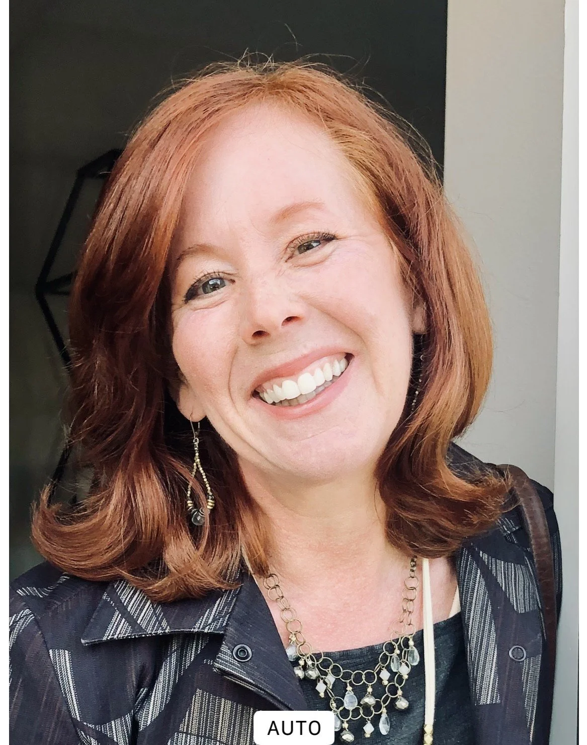 A woman with red hair smiling outdoors.
