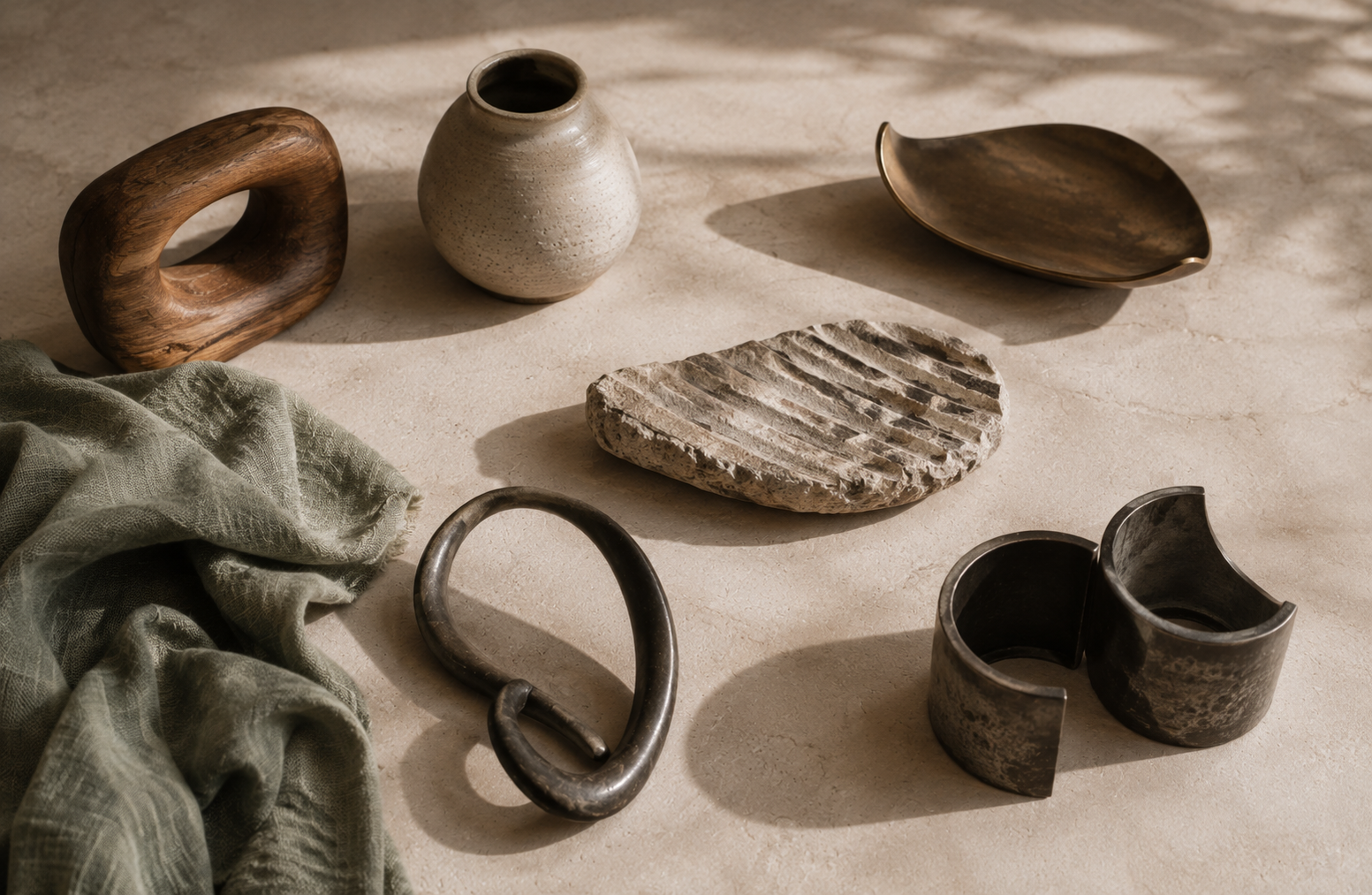 Distinct wood, ceramic, bronze, stone, forged metal, and sage textile forms share an open sunlit space, suggesting varied ways of creating connection, intimacy, autonomy, and belonging.