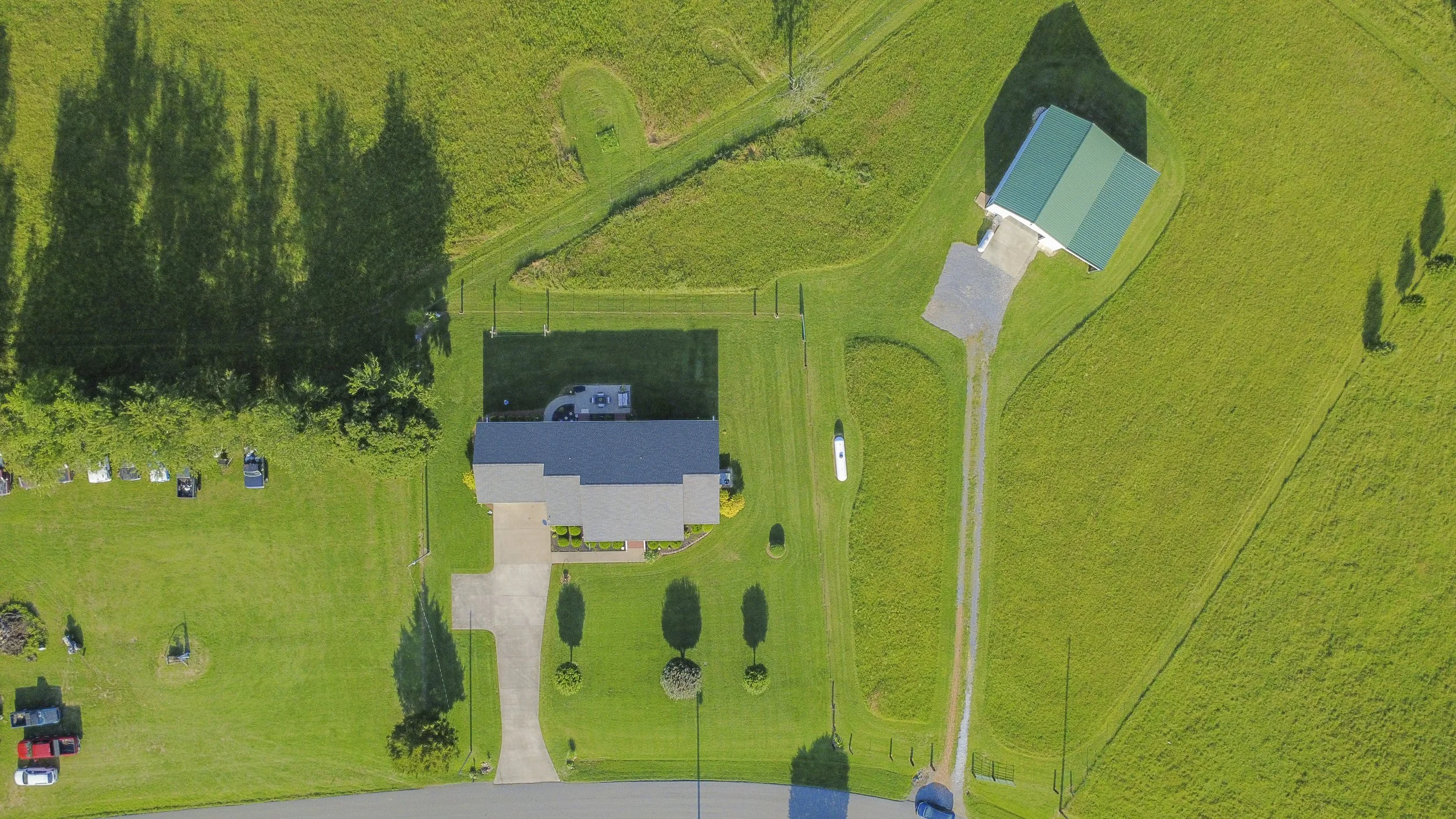 Aerial view of a green backyard with a house, trees, a driveway, and playground equipment.