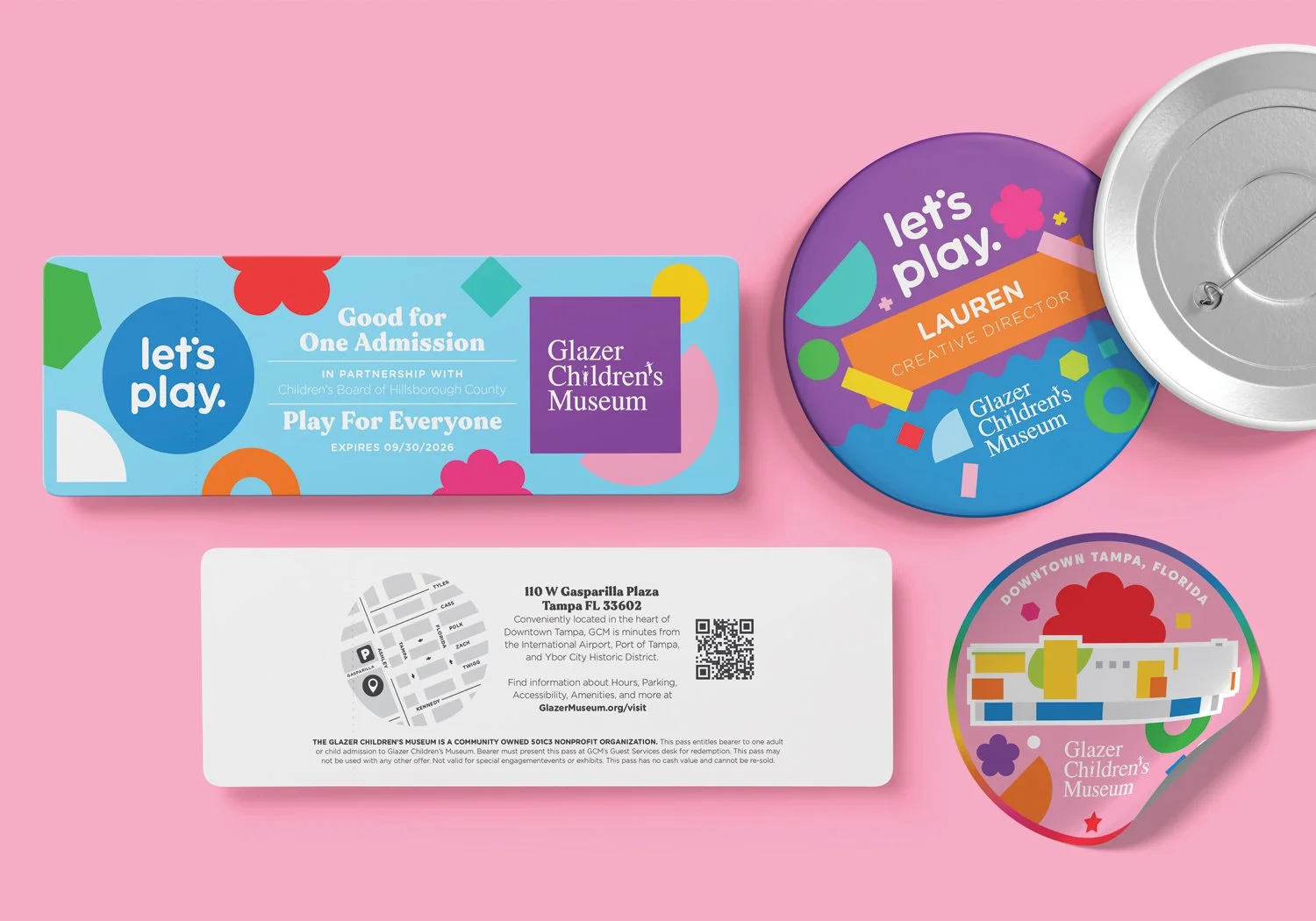A flat-lay view of printed collateral such as admission tickets, buttons, and stickers for the Glazer Children's Museum set against a pink background.