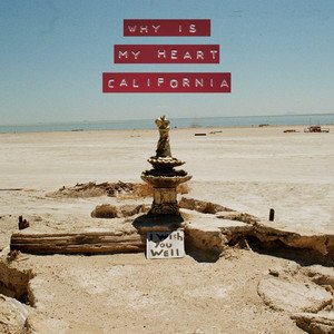 A desert beach scene with a small stone stack and a handwritten sign that says 'I wish you well.' Above, there is red text that reads 'Why is my heart California.'