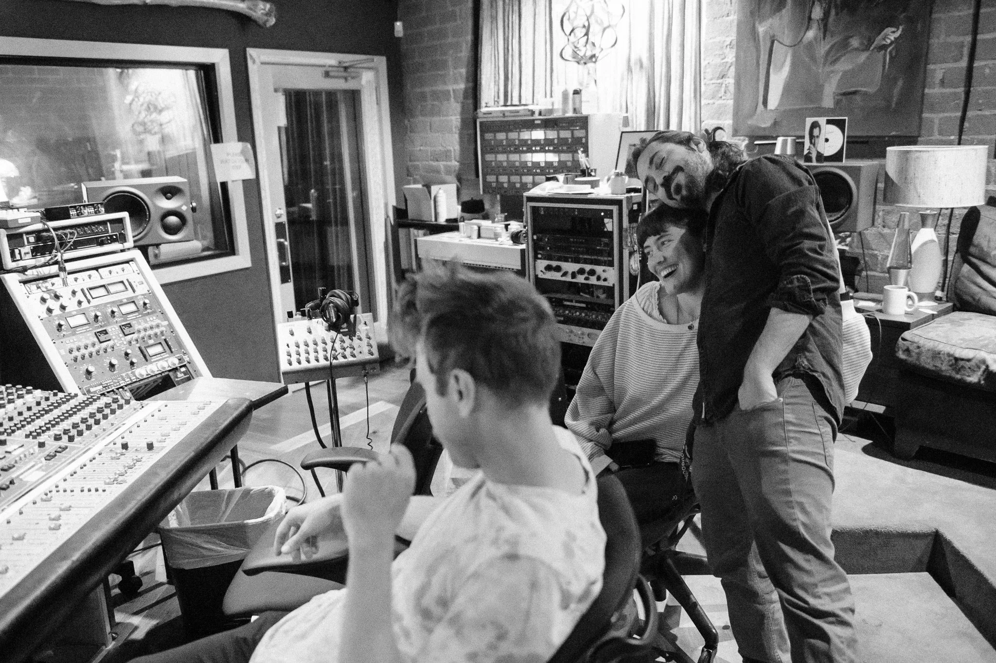 Two men and one boy in a recording studio, with audio equipment and soundproof walls, sharing a joyful moment.