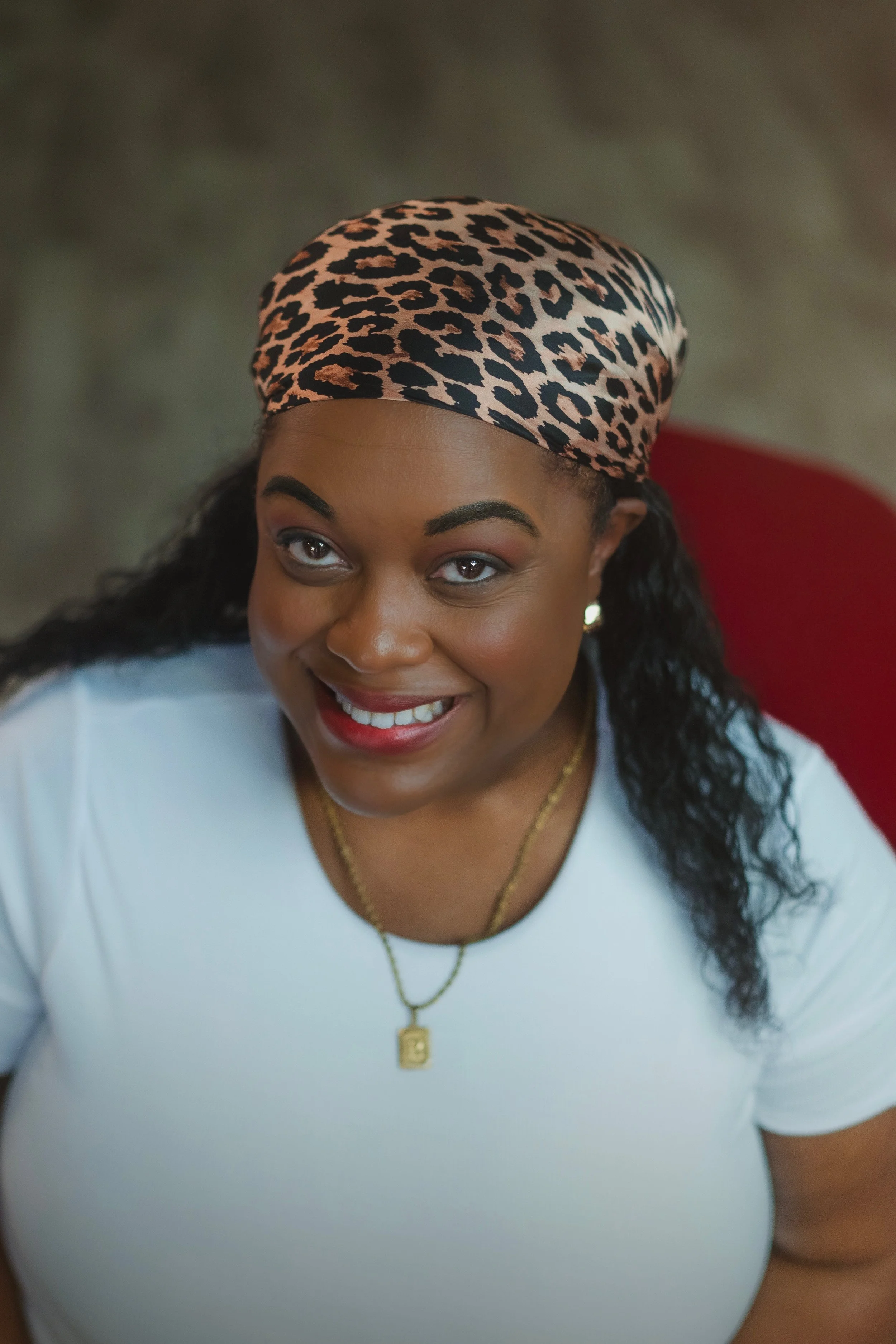 Close-up of Raquita wearing a leopard-print headscarf, white top, and gold jewelry.