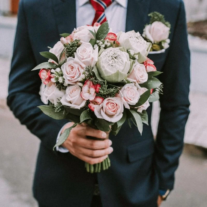 A man in a suit's torso holding a boquet of flowers.