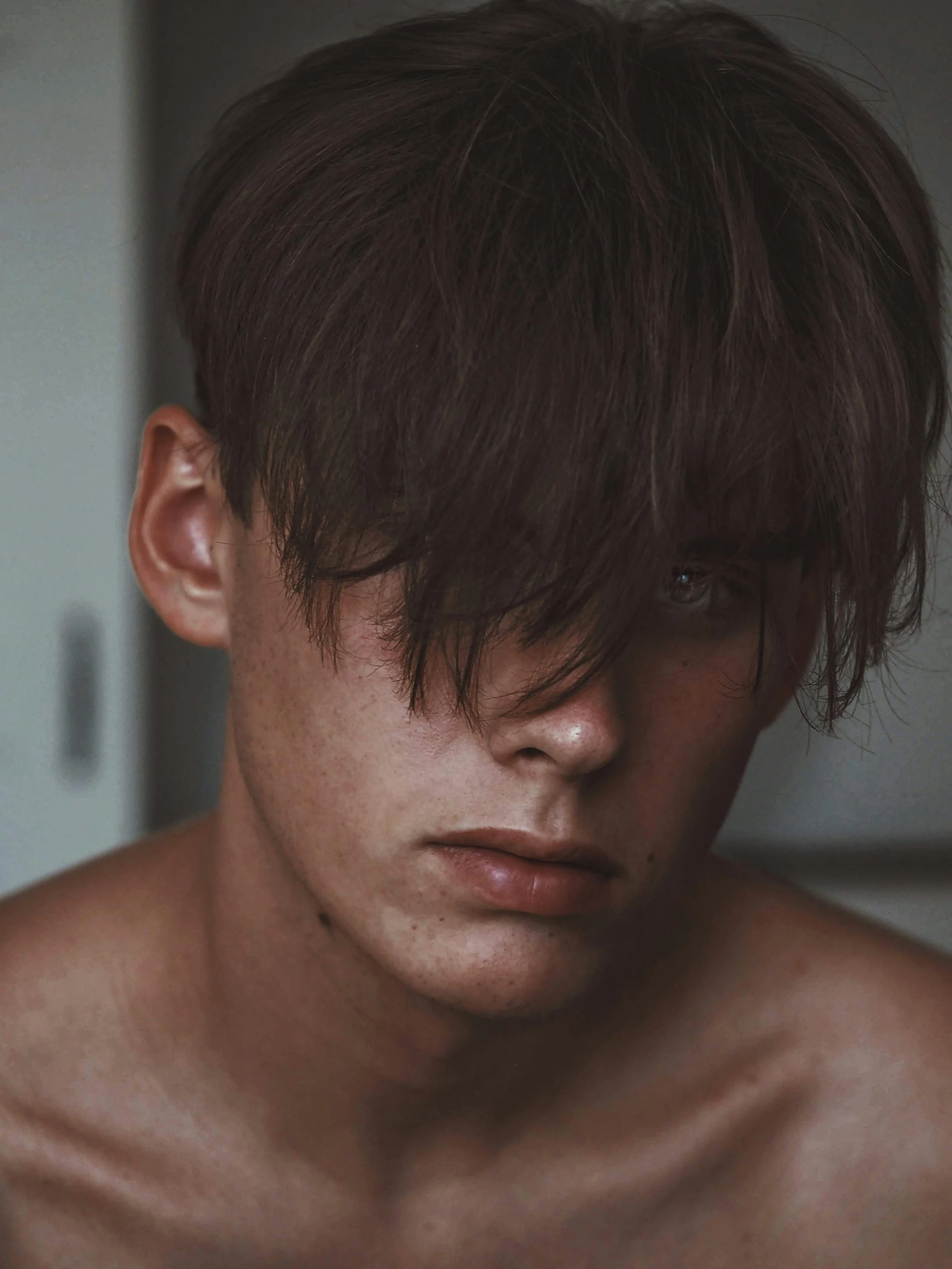 A boy with brown hair covering his eyes looking at the camera.