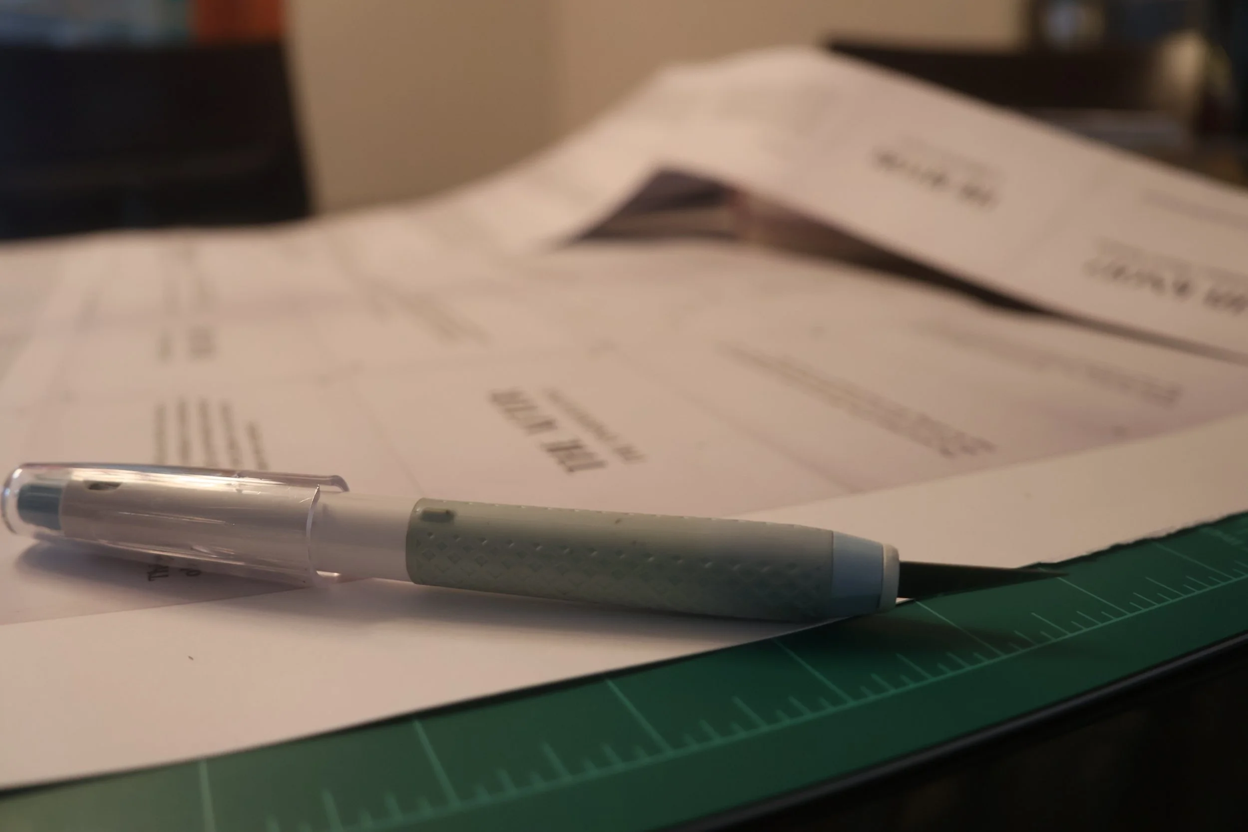 Exacto knife on top of the zine poster being cut ontop of a green cutting mat.