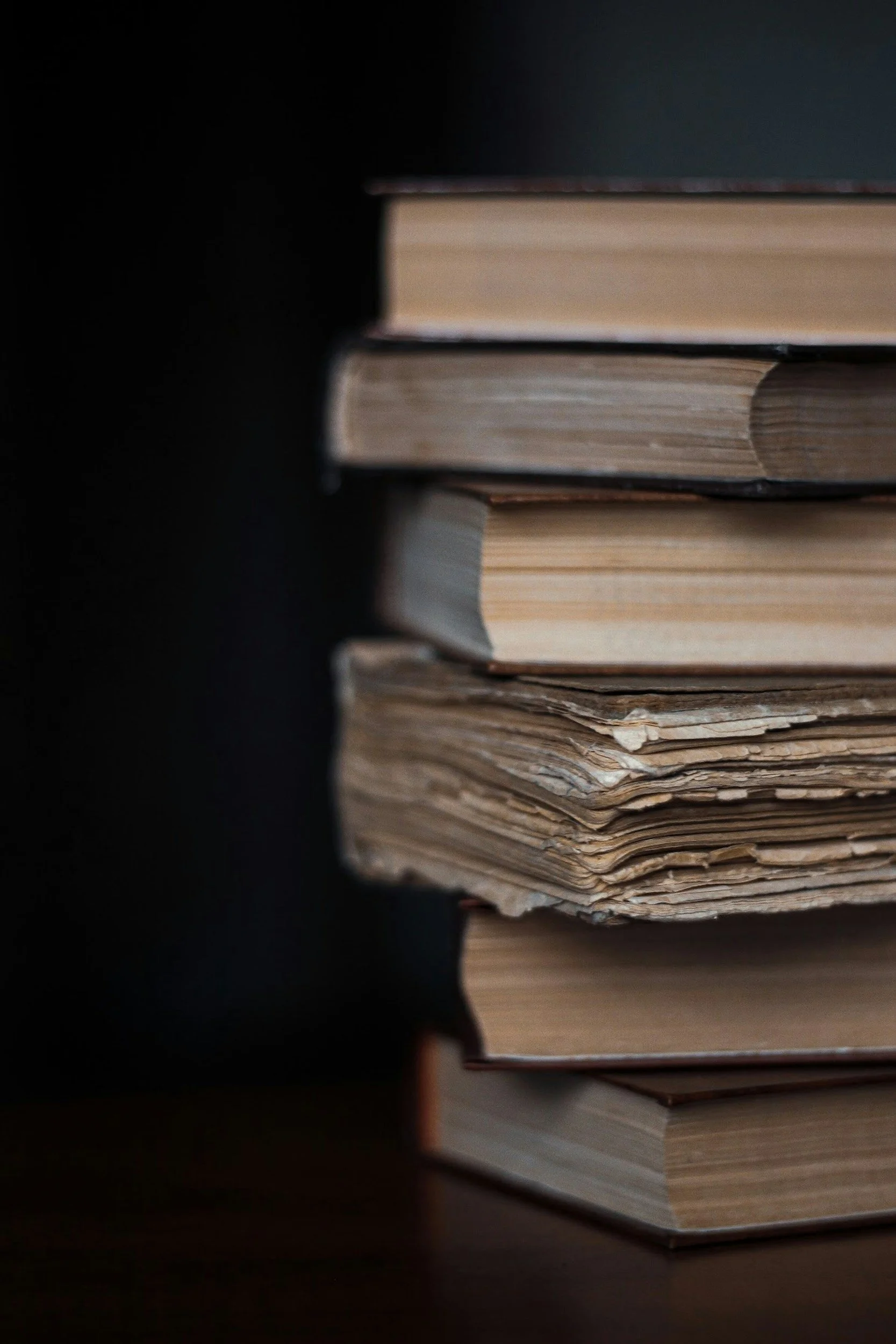 A close-up of a stack of old books with worn pages on a dark surface.