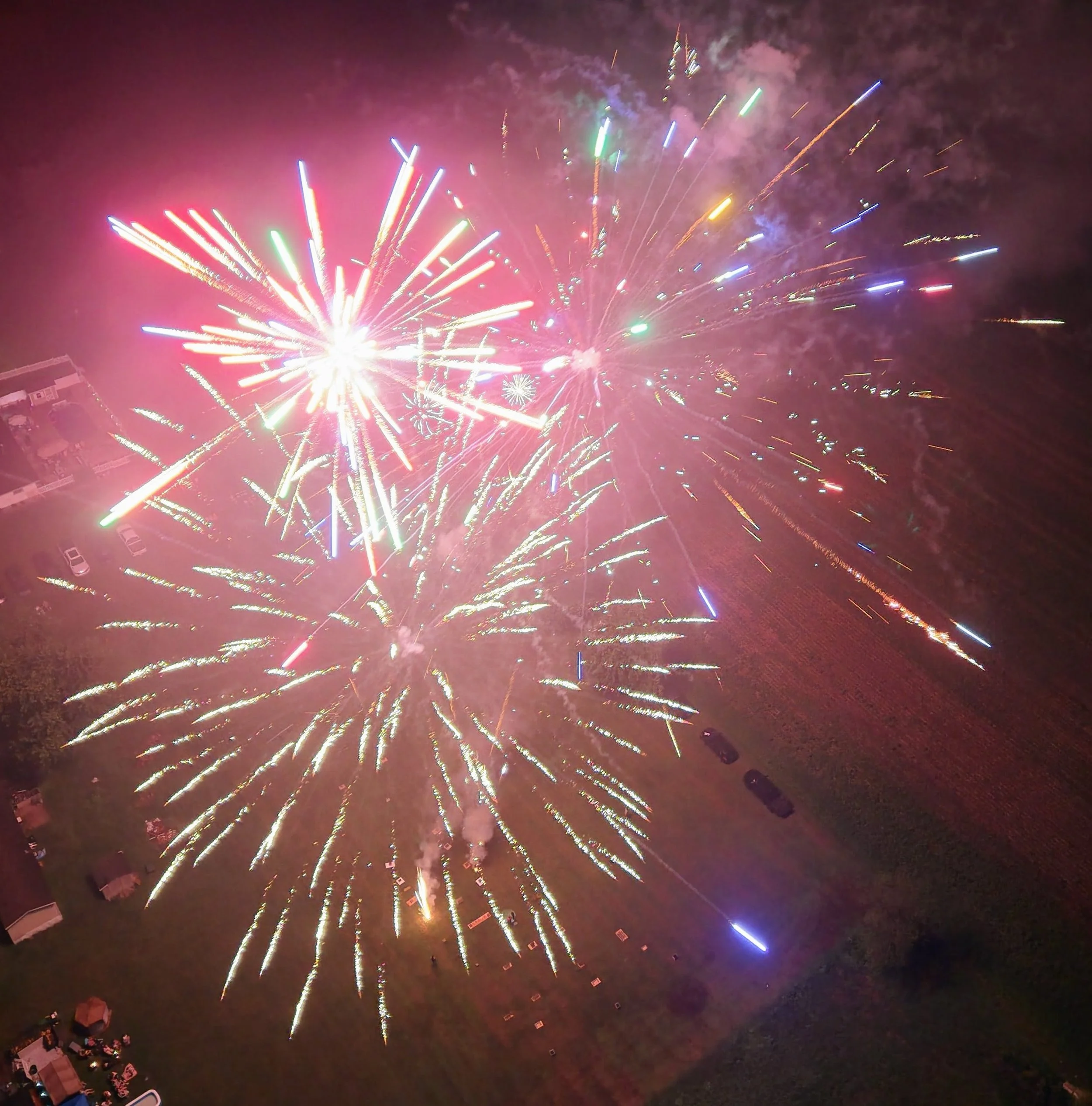 Night sky filled with colorful fireworks exploding over a residential neighborhood with visible houses and streets.