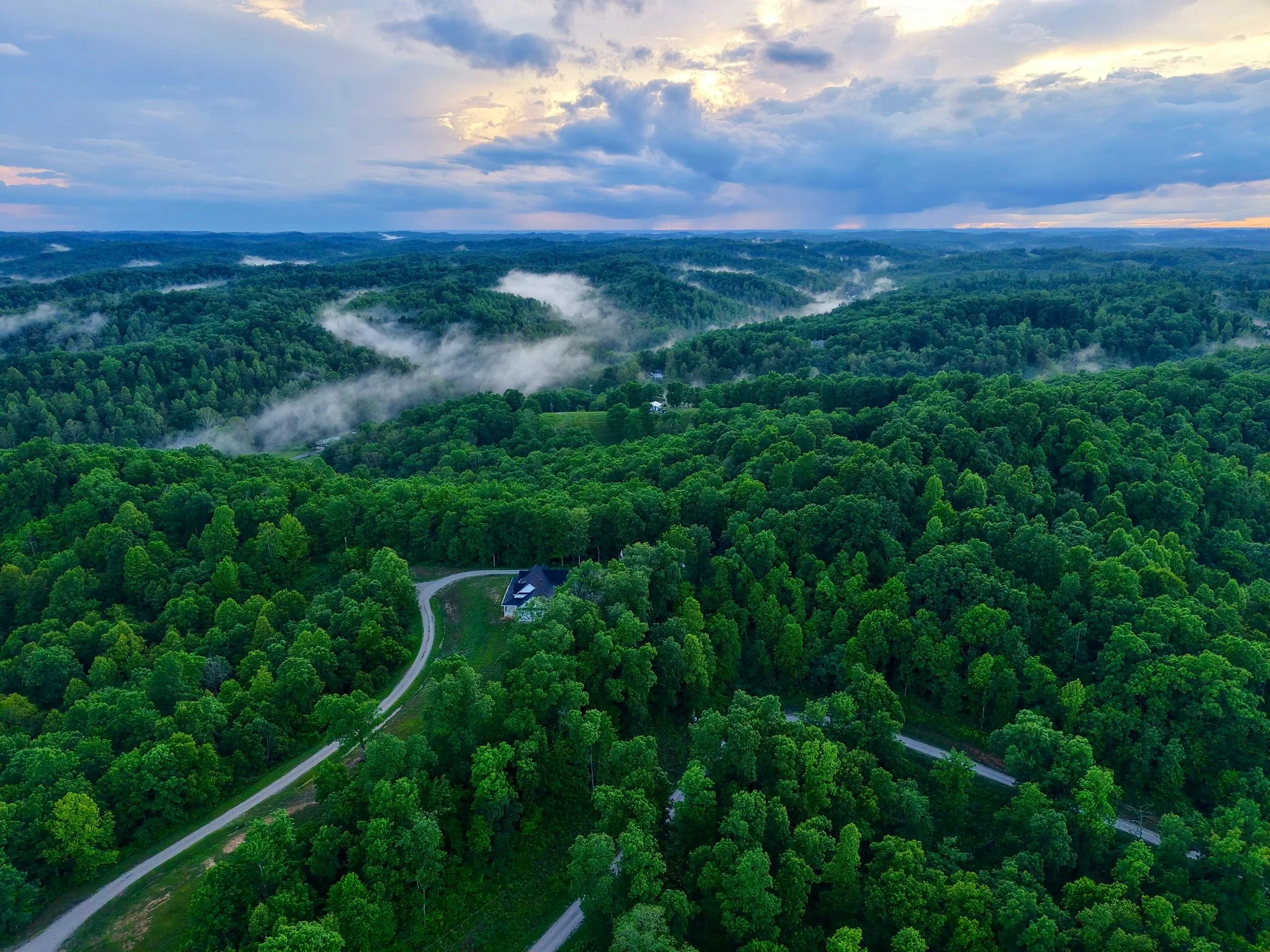 Aerial photo of mountainous terrain, fog in valleys, and a rain storm in the distance.