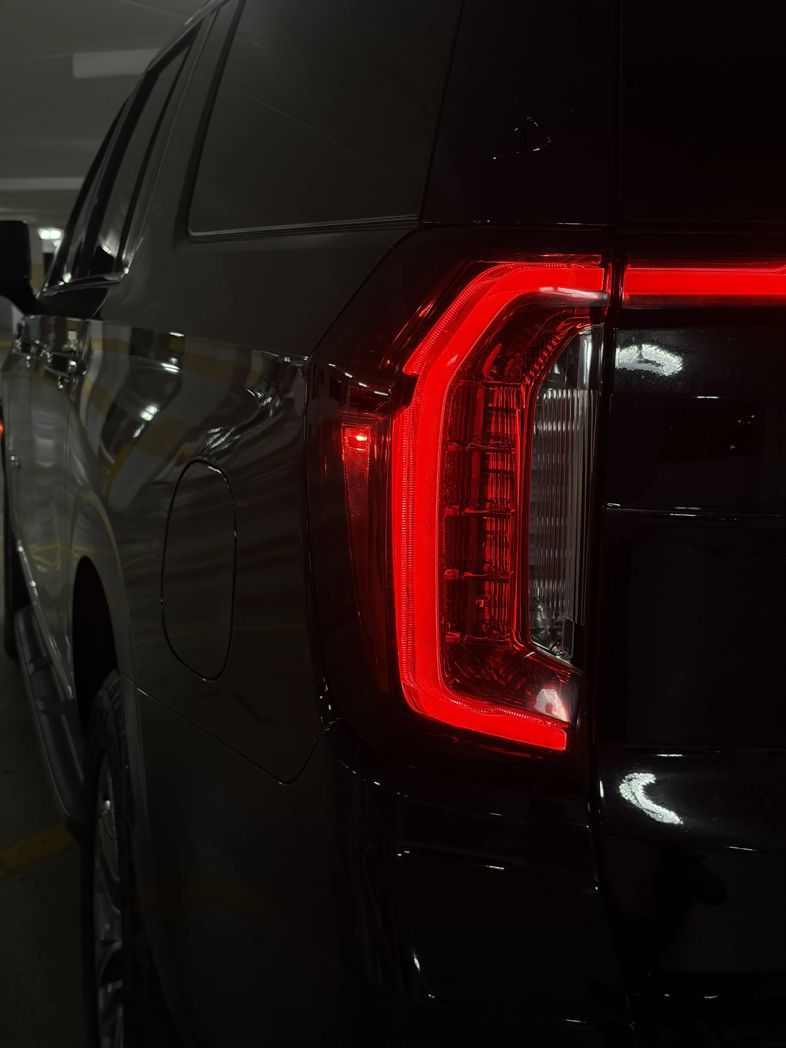 Close-up of the rear end of a black GMC Yukon showing its illuminated taillight in a parking garage at night.