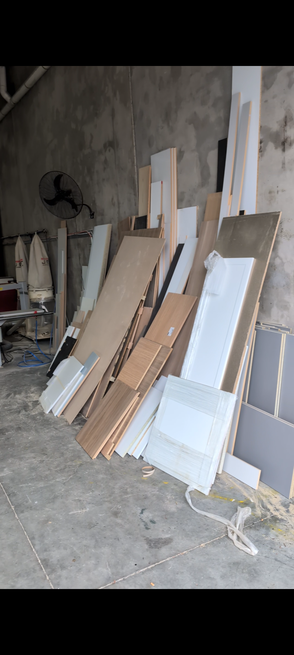 Interior construction materials stacked against a wall, including wooden and MDF panels, in a partially finished room with concrete floor and unfinished walls.
