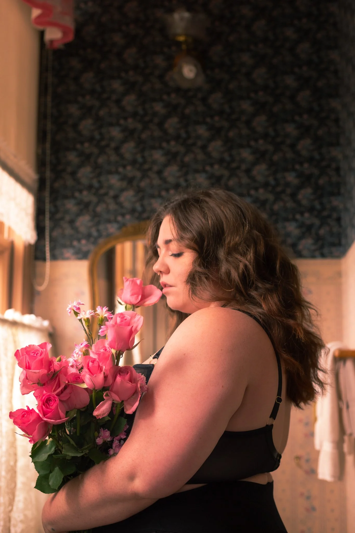 A woman with curly brown hair wearing a black dress holding a large bouquet of pink roses and other pink flowers.