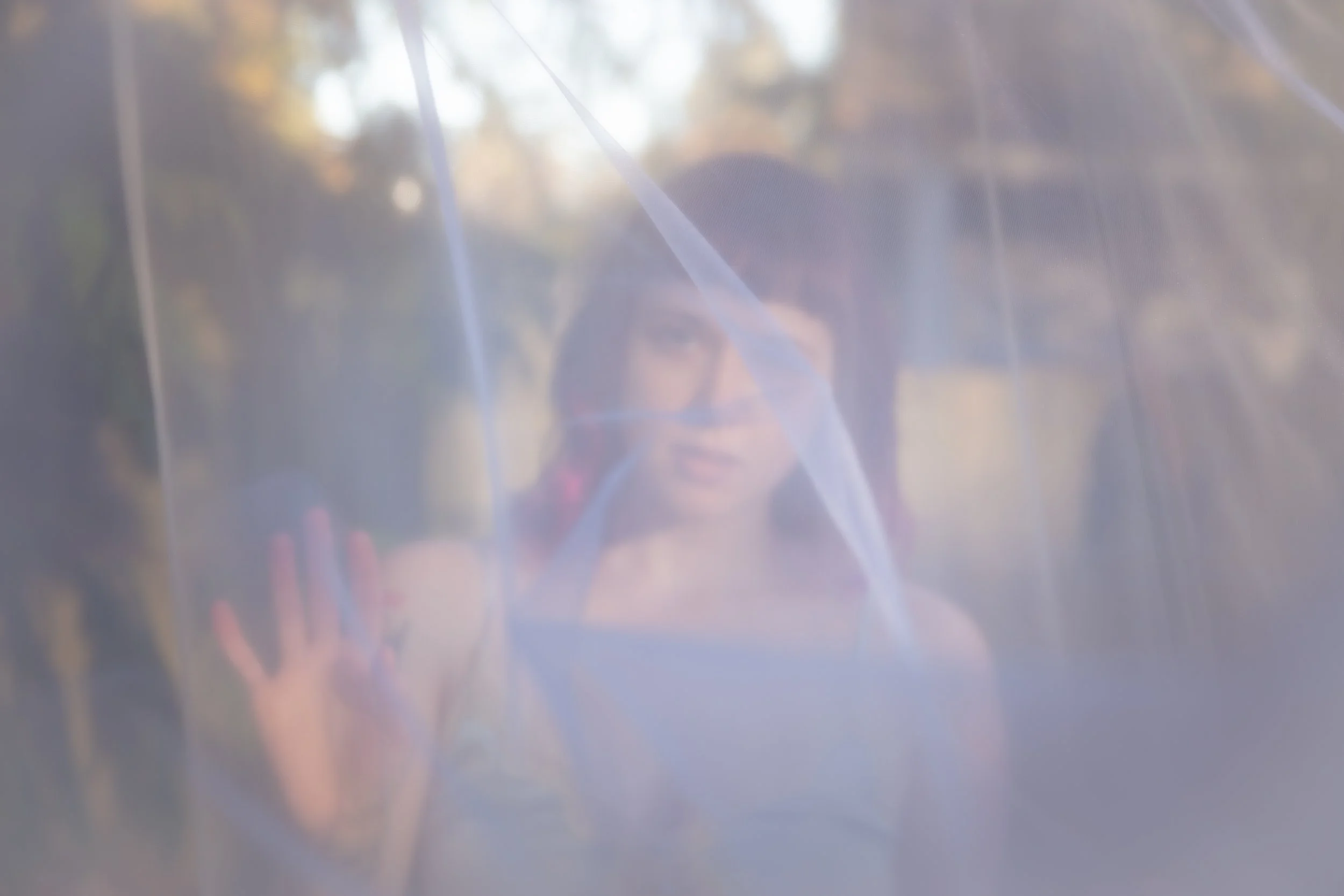 A blurred image of a person seen through a translucent surface, possibly glass or plastic, with some light reflections and shadowy background.