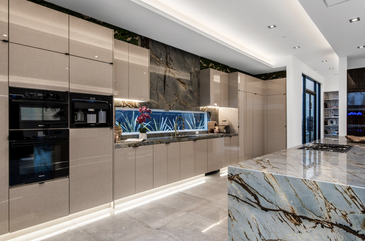 Modern kitchen with beige cabinets, marble countertops, a blue decorative backsplash, and built-in appliances.