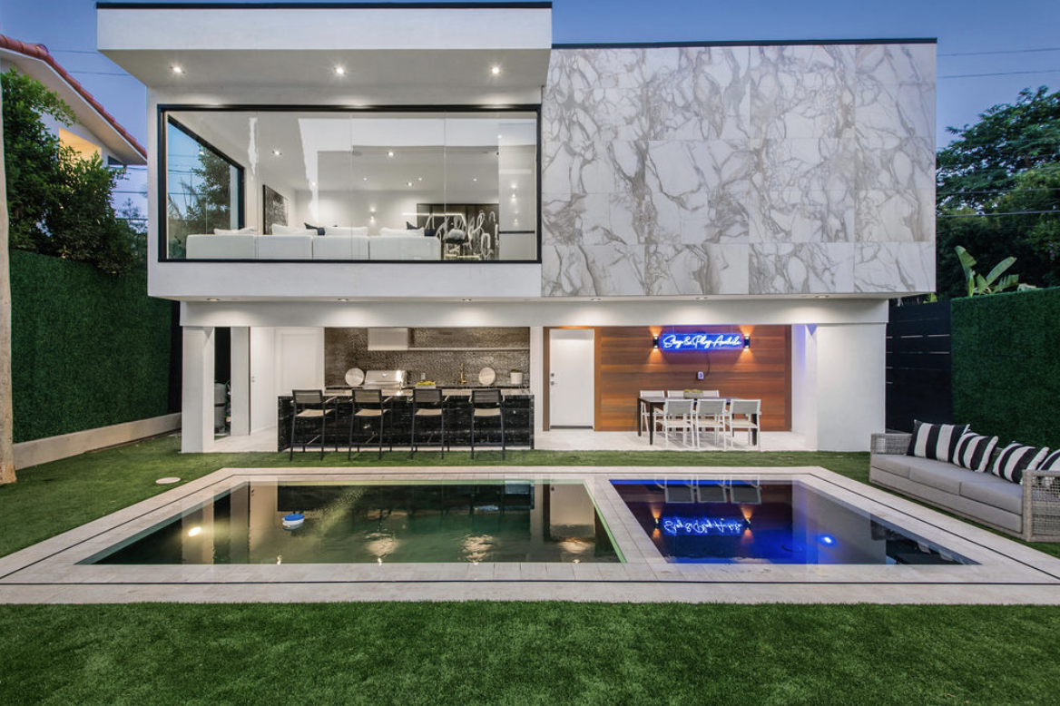 Modern house with a backyard featuring a swimming pool, outdoor seating, and an illuminated sign on the wall reading "Buy & Sell."