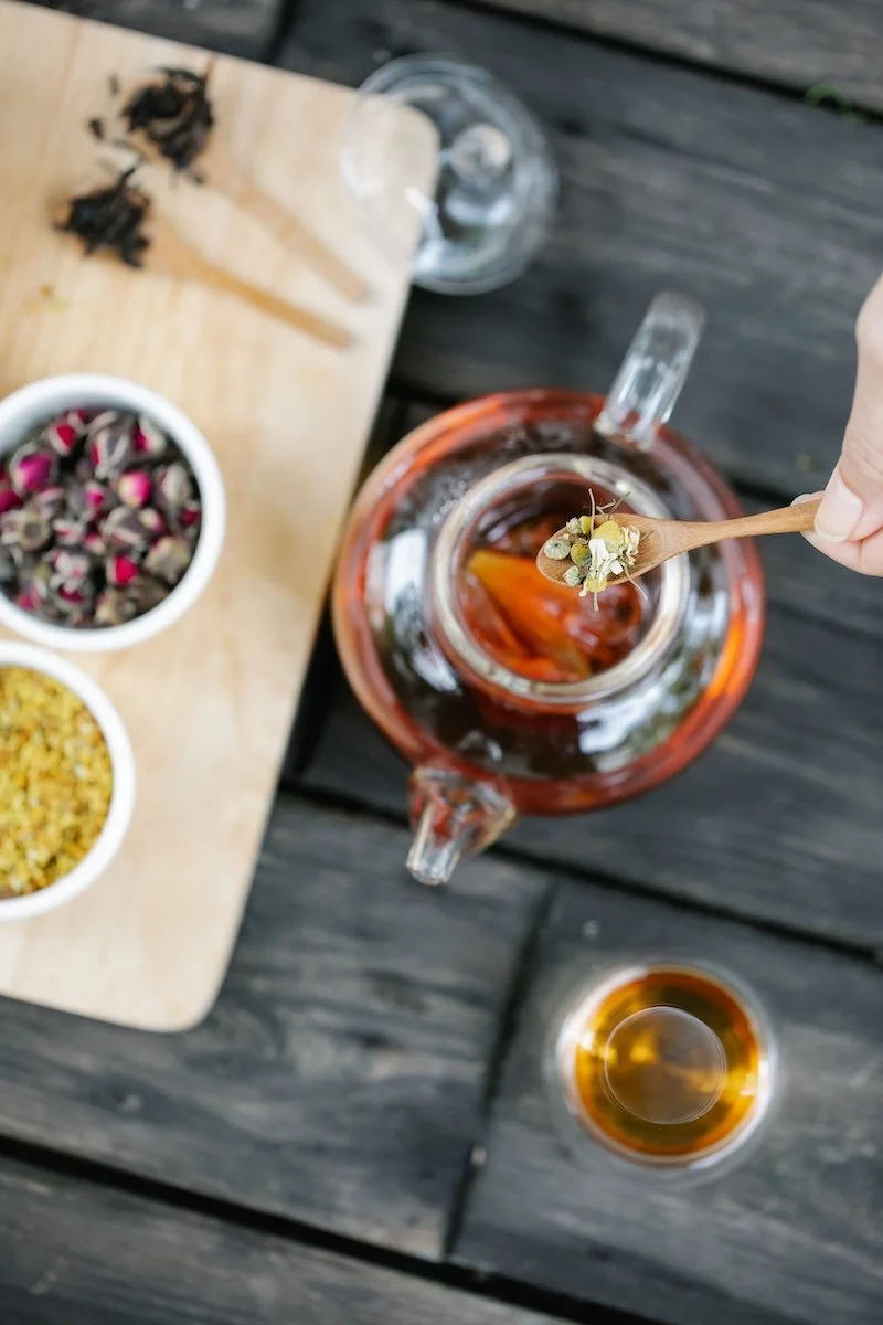 Herbal tea being poured with dried herbs and flowers on a wooden table — naturopathic herbal medicine