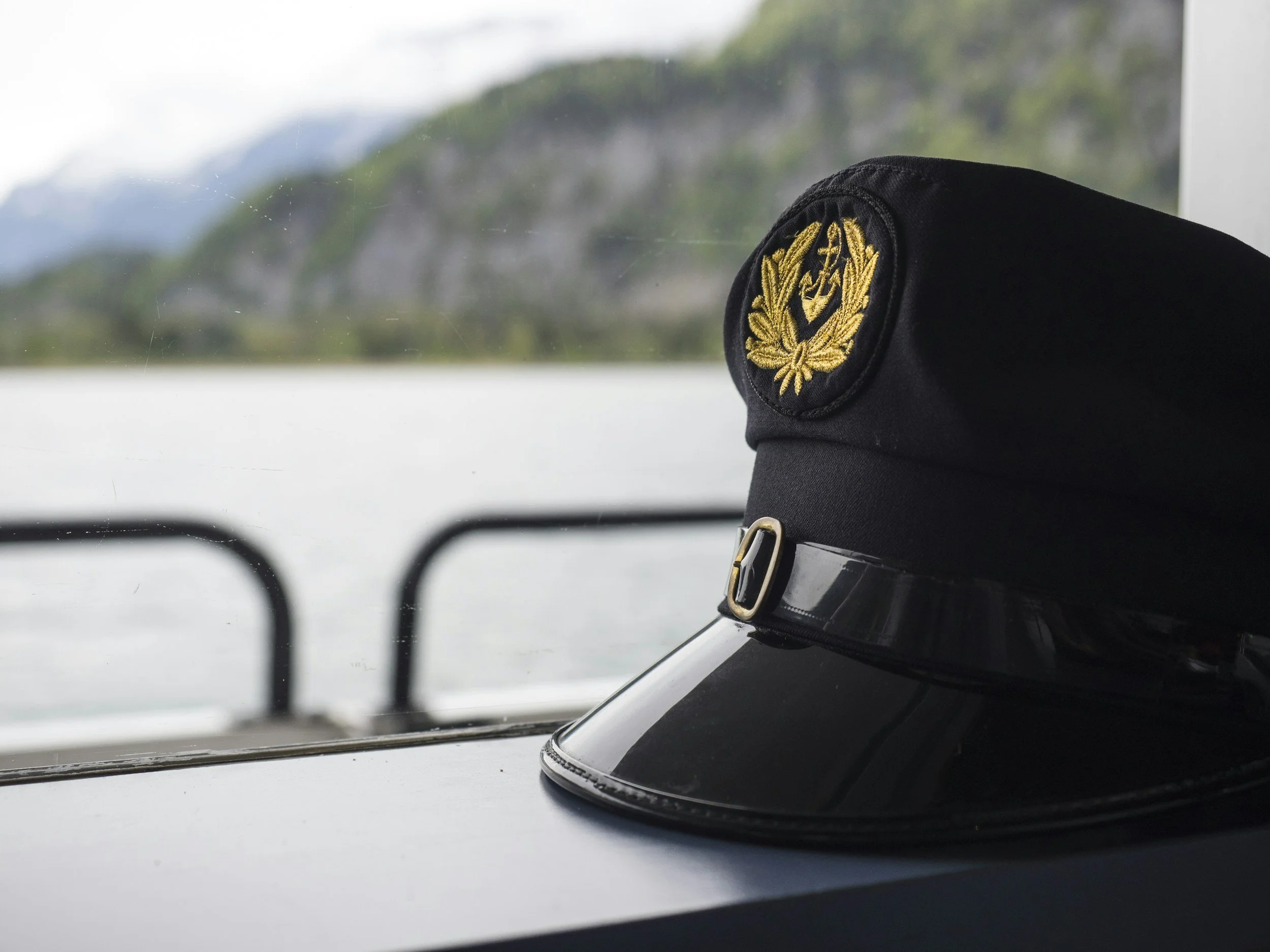Captain cap with gold emblem placed on a helm, looking out the window at a blurred natural landscape.