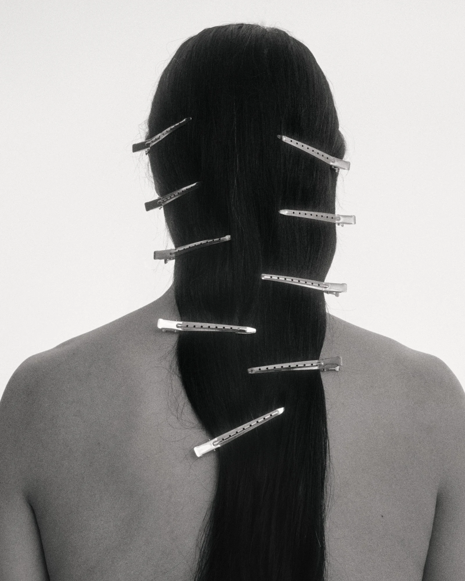 Back of a person with long dark hair, secured with hair clips against a plain background.