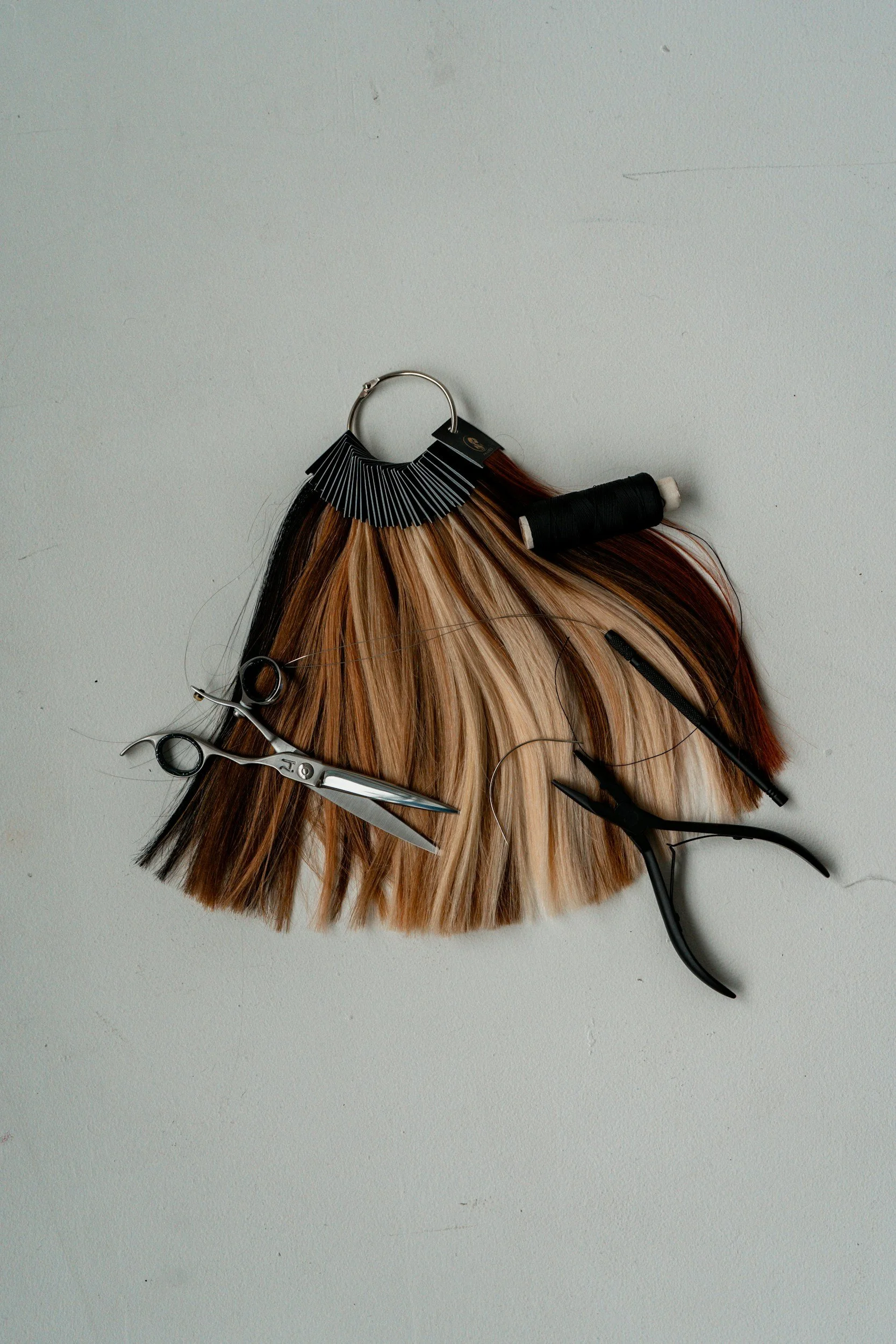 Hair color swatch fan, scissors, sectioning clips, and a styling comb on a white surface, used for hair styling or coloring.